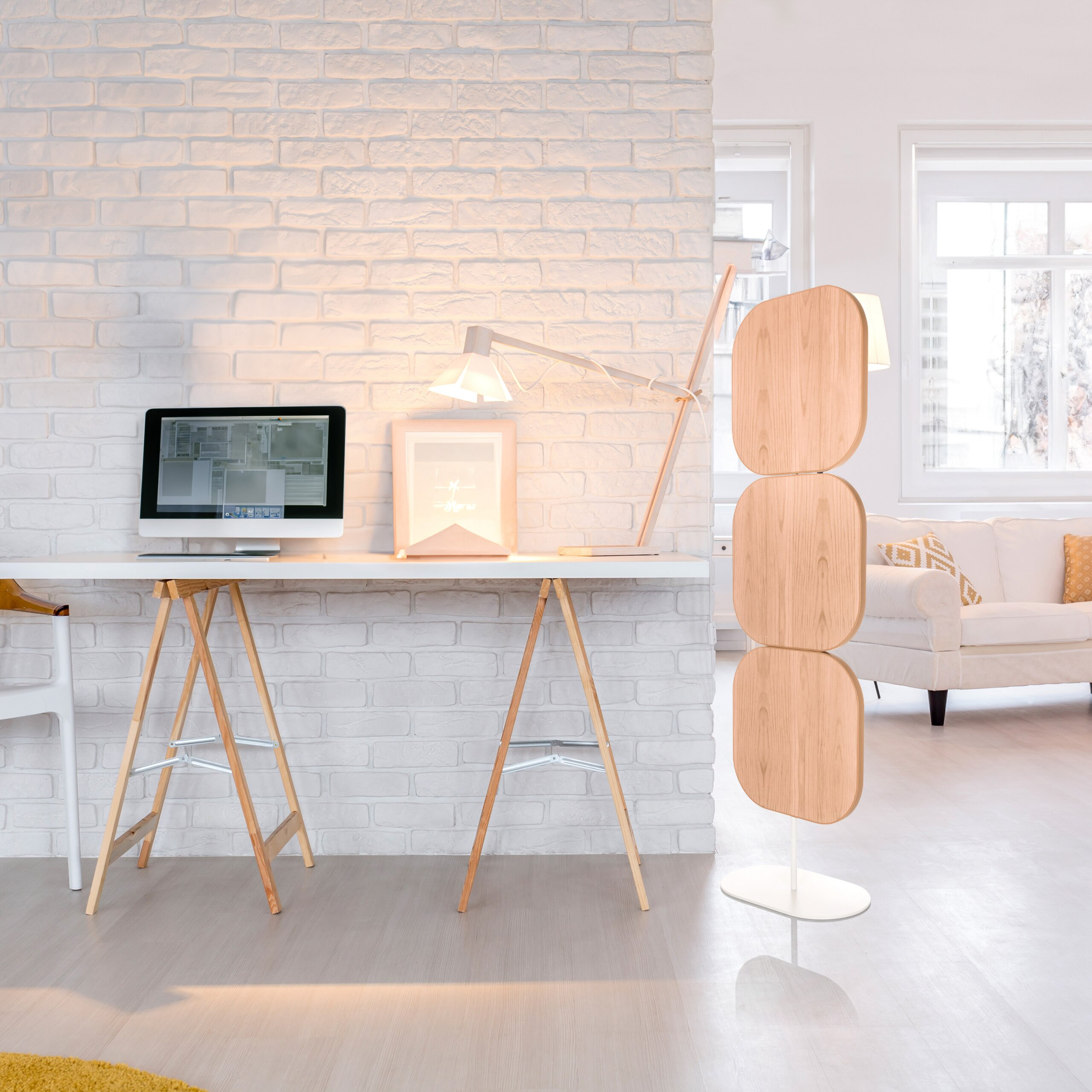 Moderne Arbeitsplatz mit weißem Schreibtisch, Computer, Lampe vor einer weißen Backsteinwand und heller Wohnbereich.