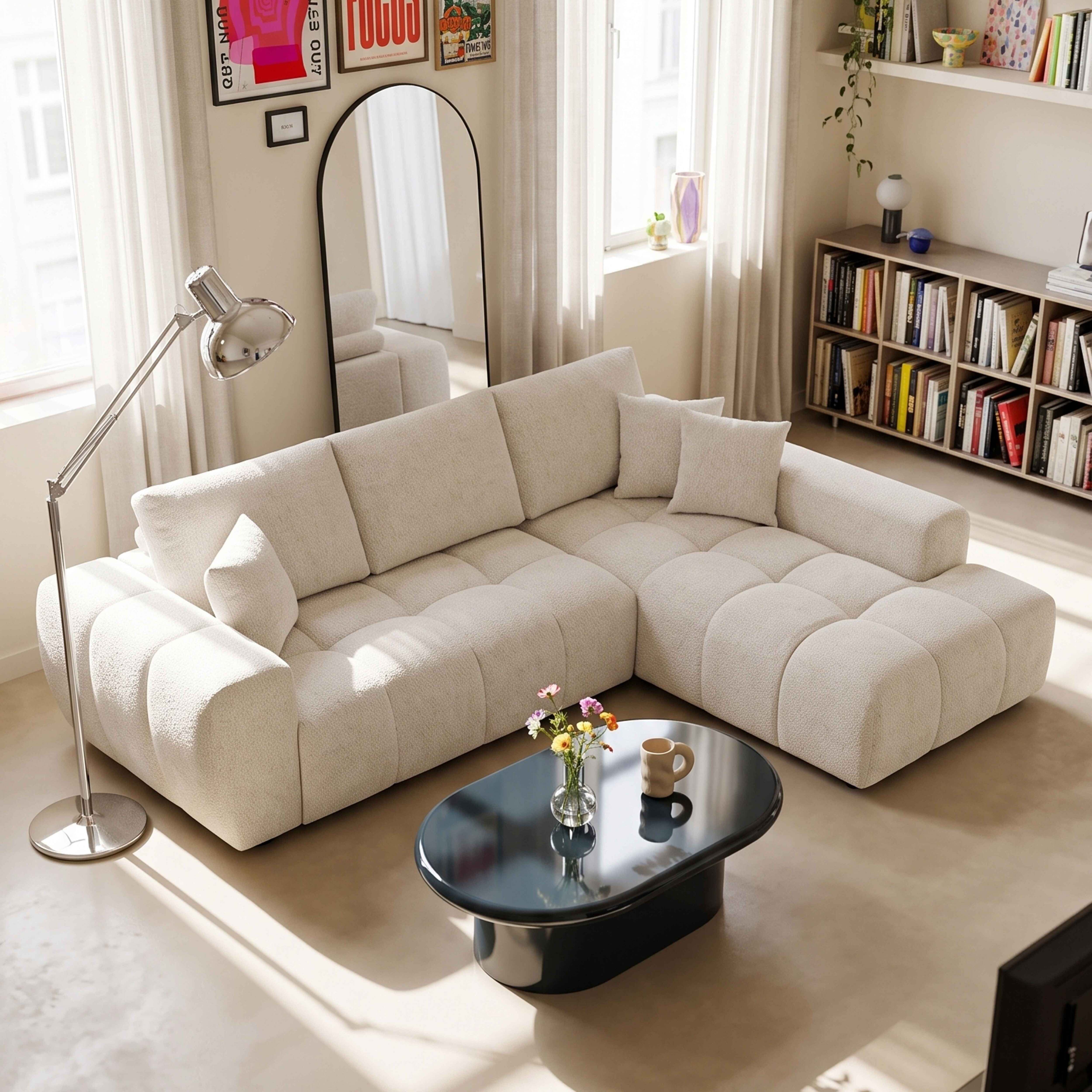 Ein helles, modernes Wohnzimmer mit großem beigen Sofa, schwarzem Couchtisch und Bücherregal im Hintergrund.