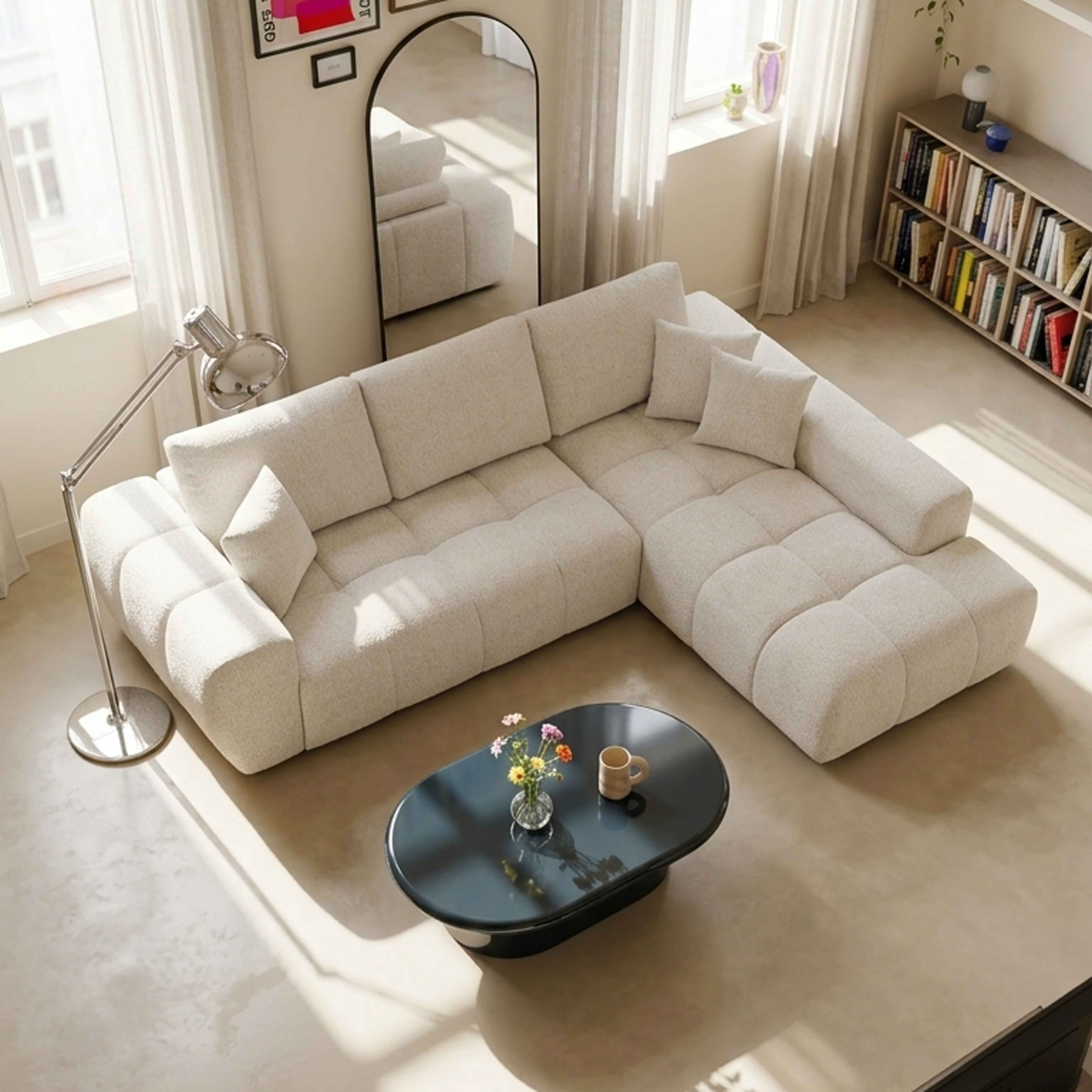 Ein helles, modernes Wohnzimmer mit einem beigen Ecksofa, einem schwarzen Tisch und einem großen Bücherregal.