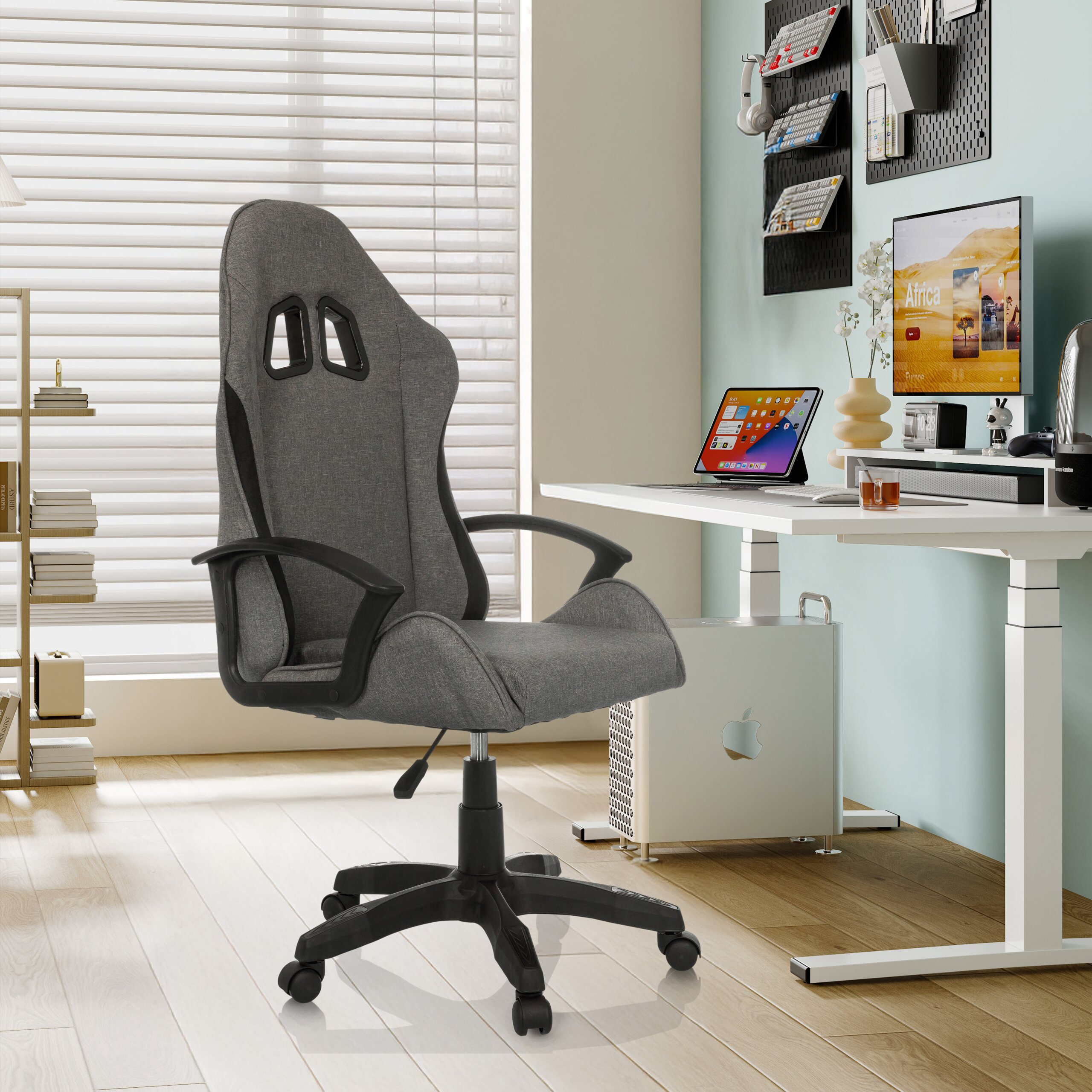 Ein grauer Gaming-Stuhl steht in einem modernen Büro vor einem weißen Schreibtisch mit Computer.