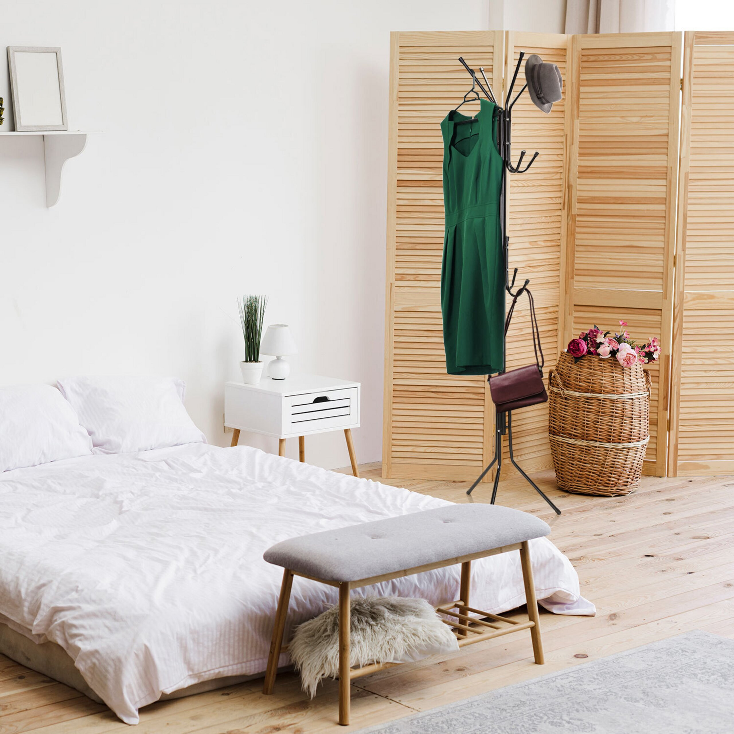 Ein helles Schlafzimmer mit weißem Bett, Holzboden, Kleiderständer mit grünem Kleid und einem Paravent im Hintergrund.