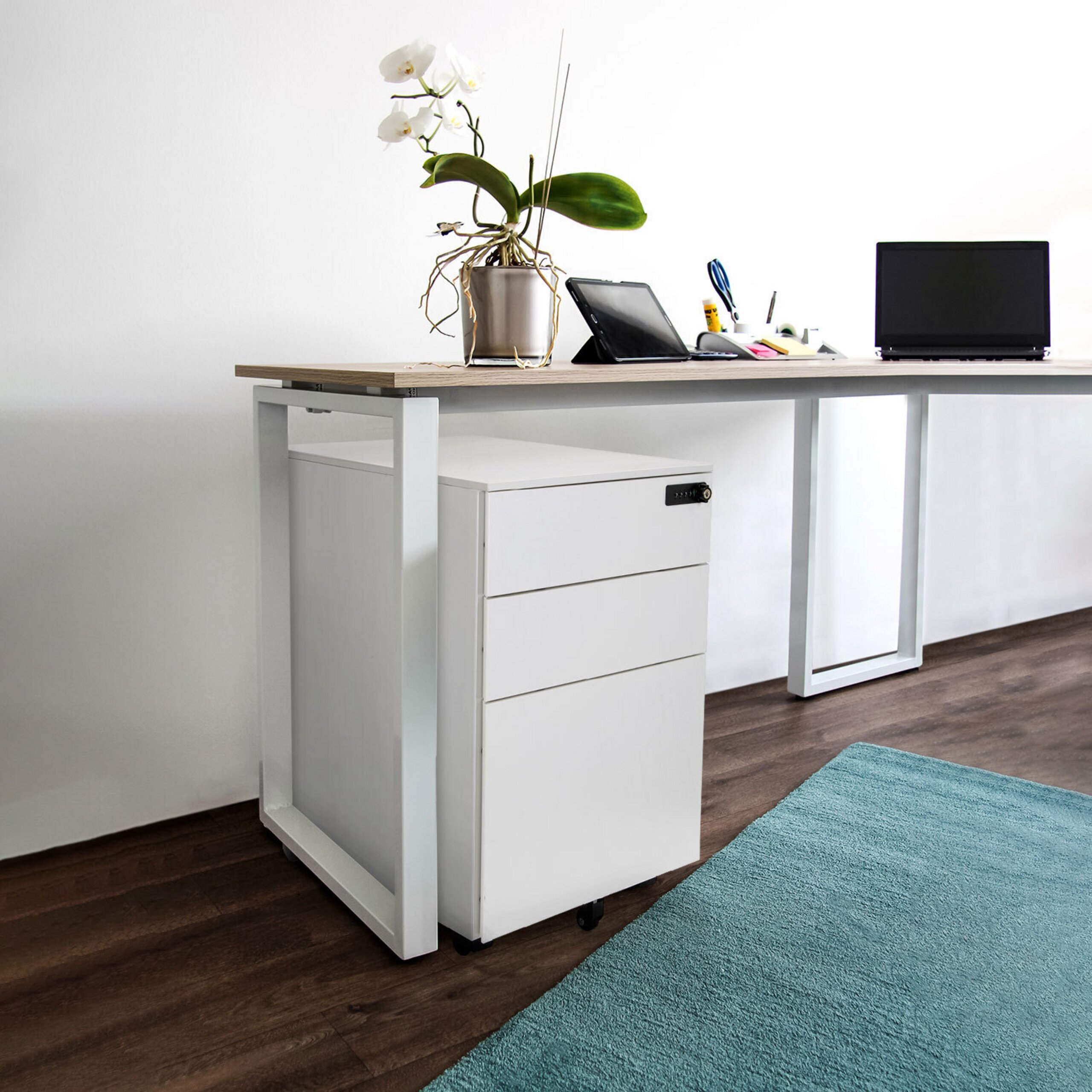 Moderner Holztisch mit weißem Gestell, Laptop, Tablet, weißem Rollcontainer und Orchidee in hellem Zimmer.