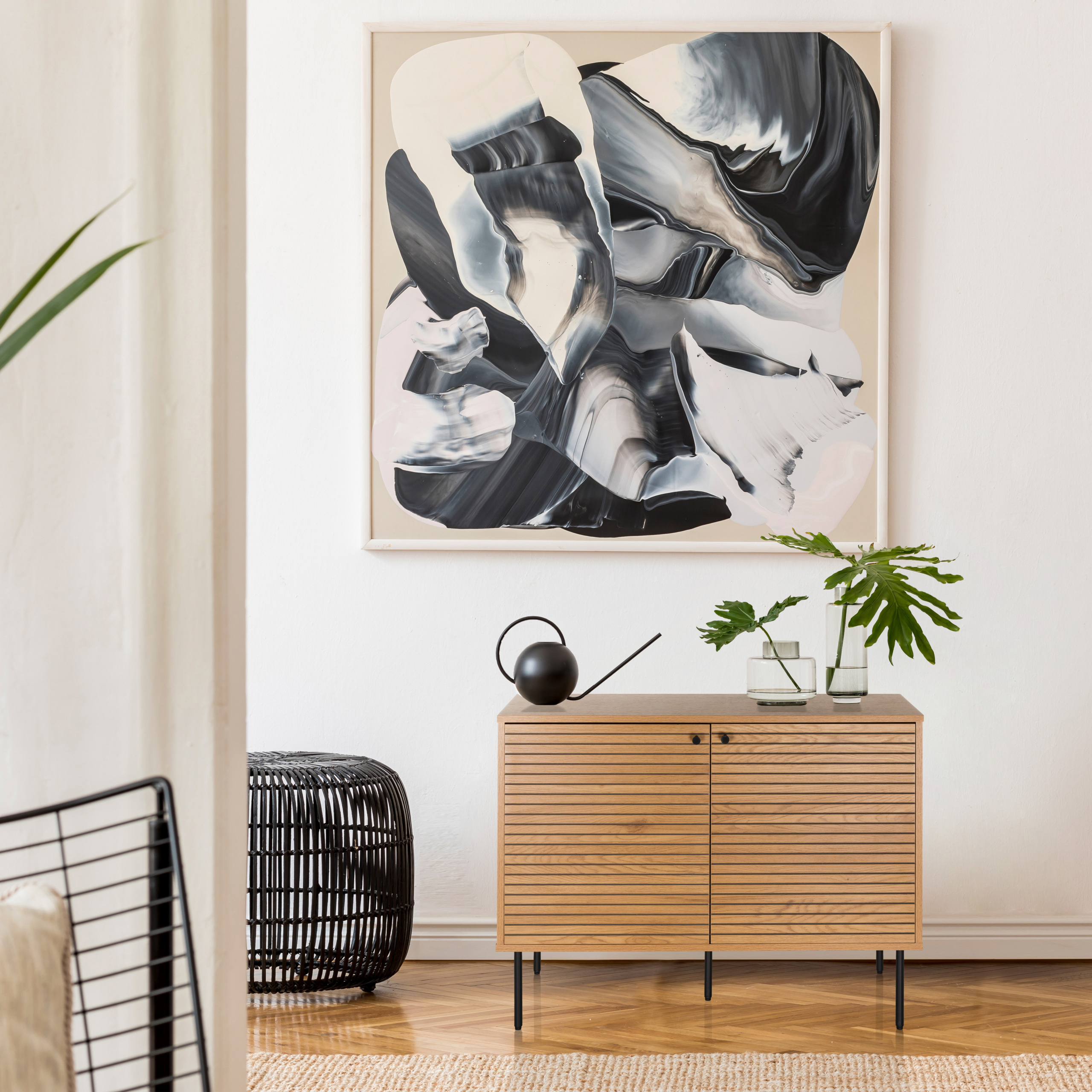 Ein hölzernes Sideboard mit Pflanzen und einer Gießkanne steht unter einem abstrakten Gemälde.