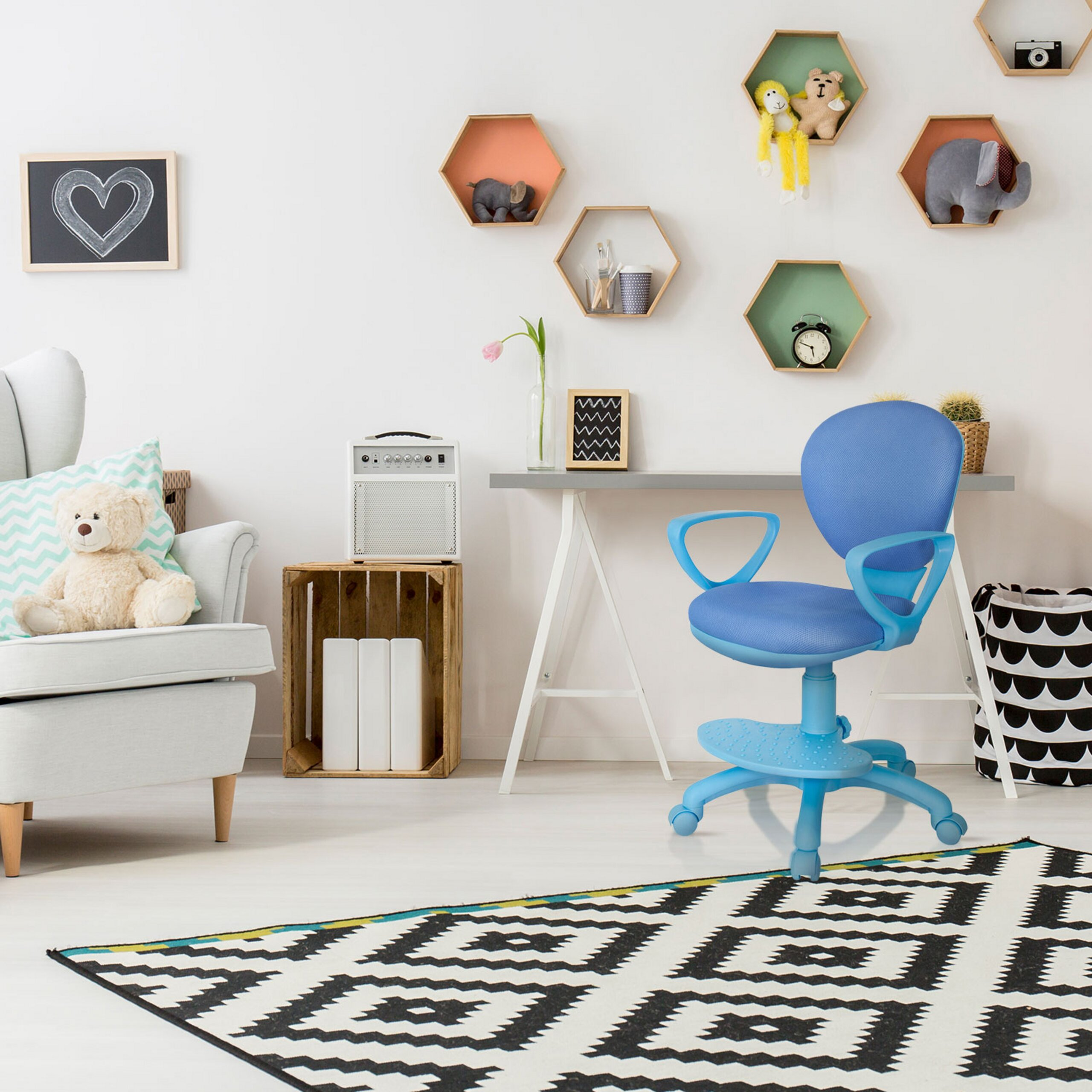 Ein Kinderzimmer mit einem blauen Stuhl, einem grauen Sessel mit Teddybär, hexagonalen Regalen und gemustertem Teppich.