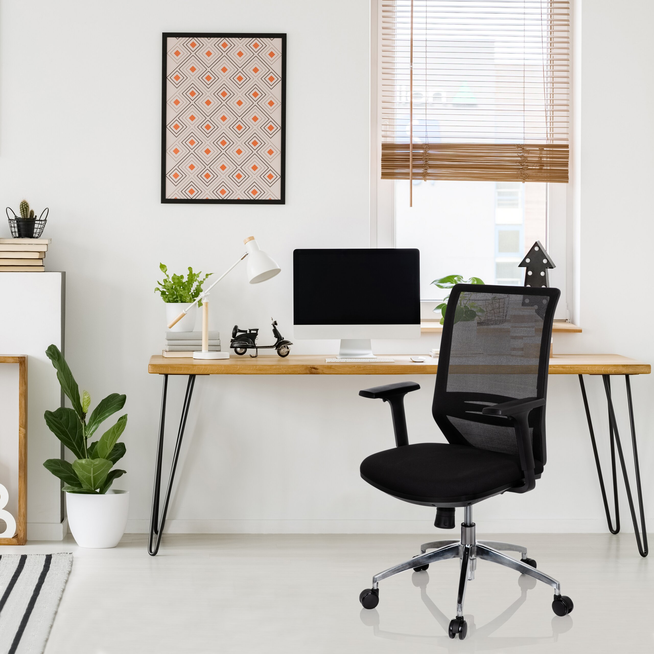 Moderne Schreibtischecke mit Computer, schwarzem Stuhl, Pflanzen, Lampe und gerahmtem Bild vor einem Fenster.