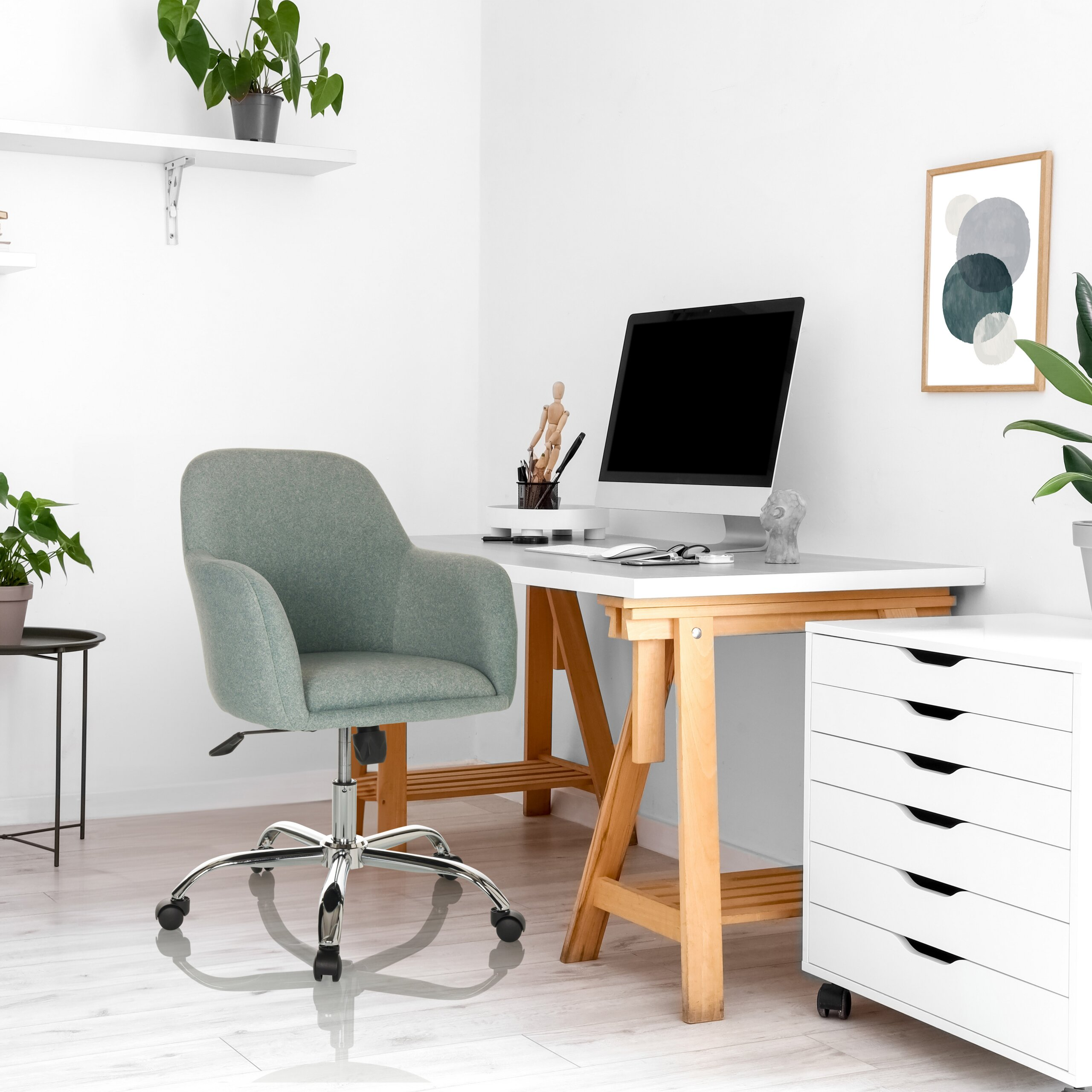 Ein weißes Heimbüro mit Holztisch, grauem Drehstuhl, Computer, Rollcontainer und Topfpflanzen.