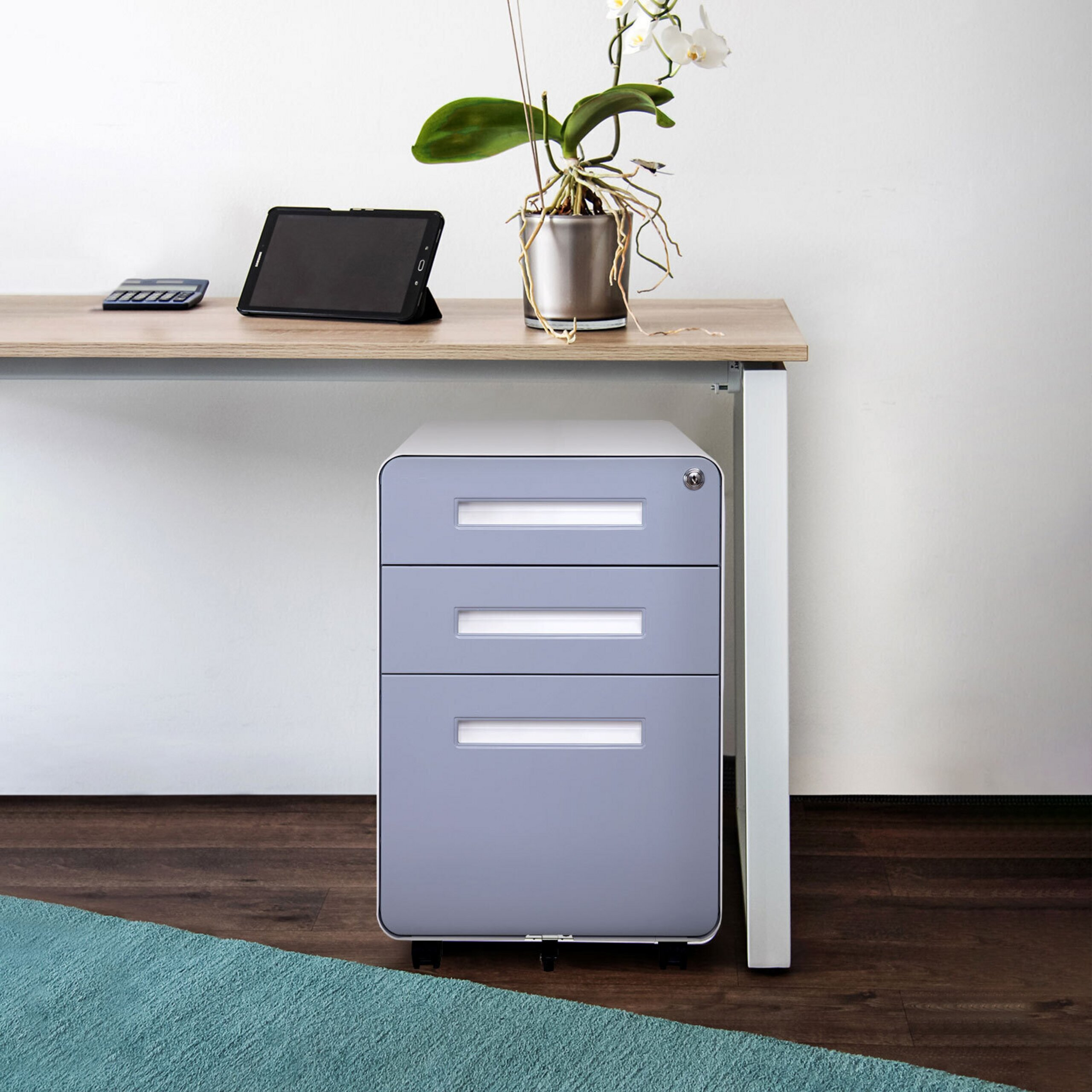 Ein grauer Rollcontainer unter einem Holztisch mit Tablet und Pflanze.