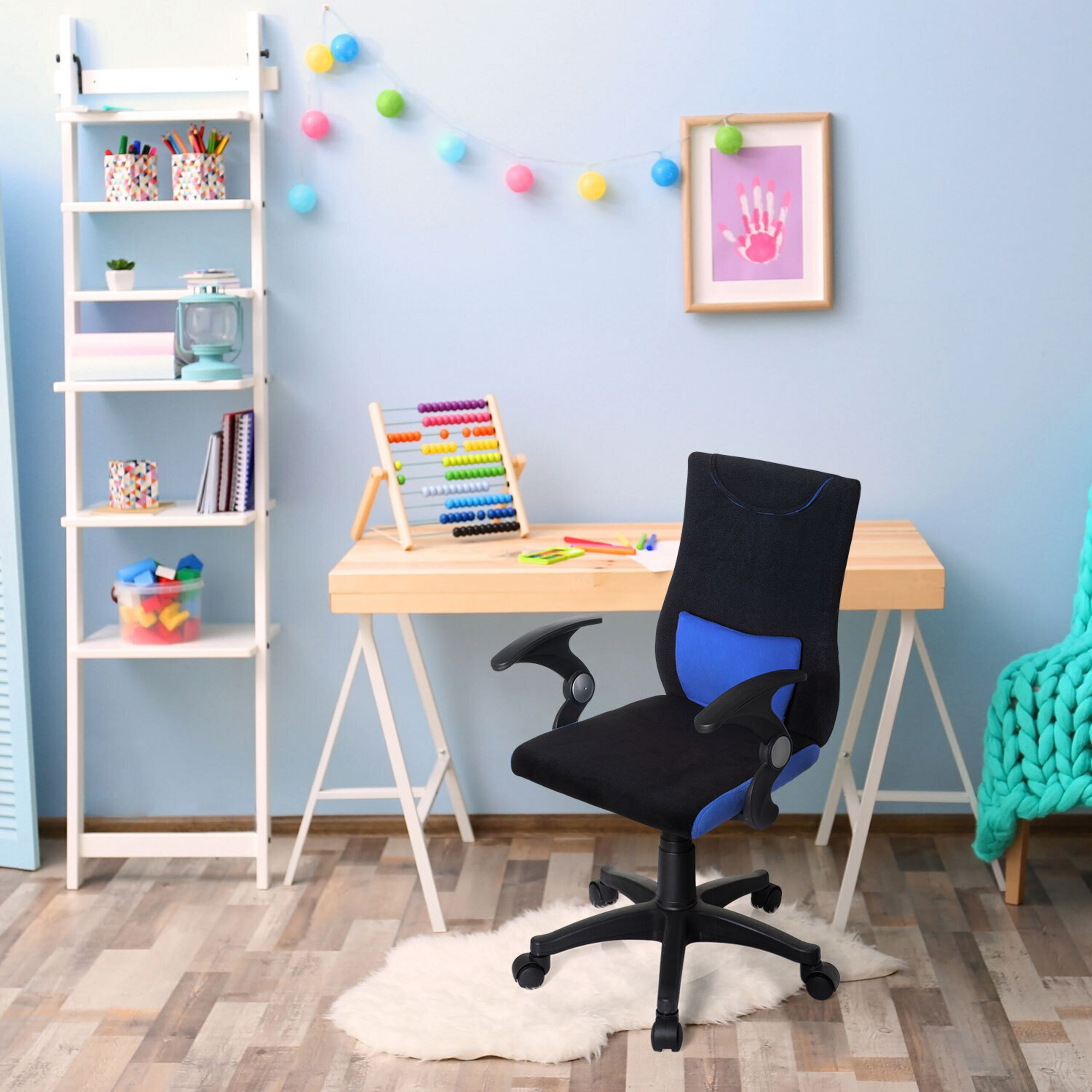 Ein schwarzer und blauer Schreibtischstuhl steht in einem bunten Kinderzimmer mit hellem Holzschreibtisch und weißem Regal.