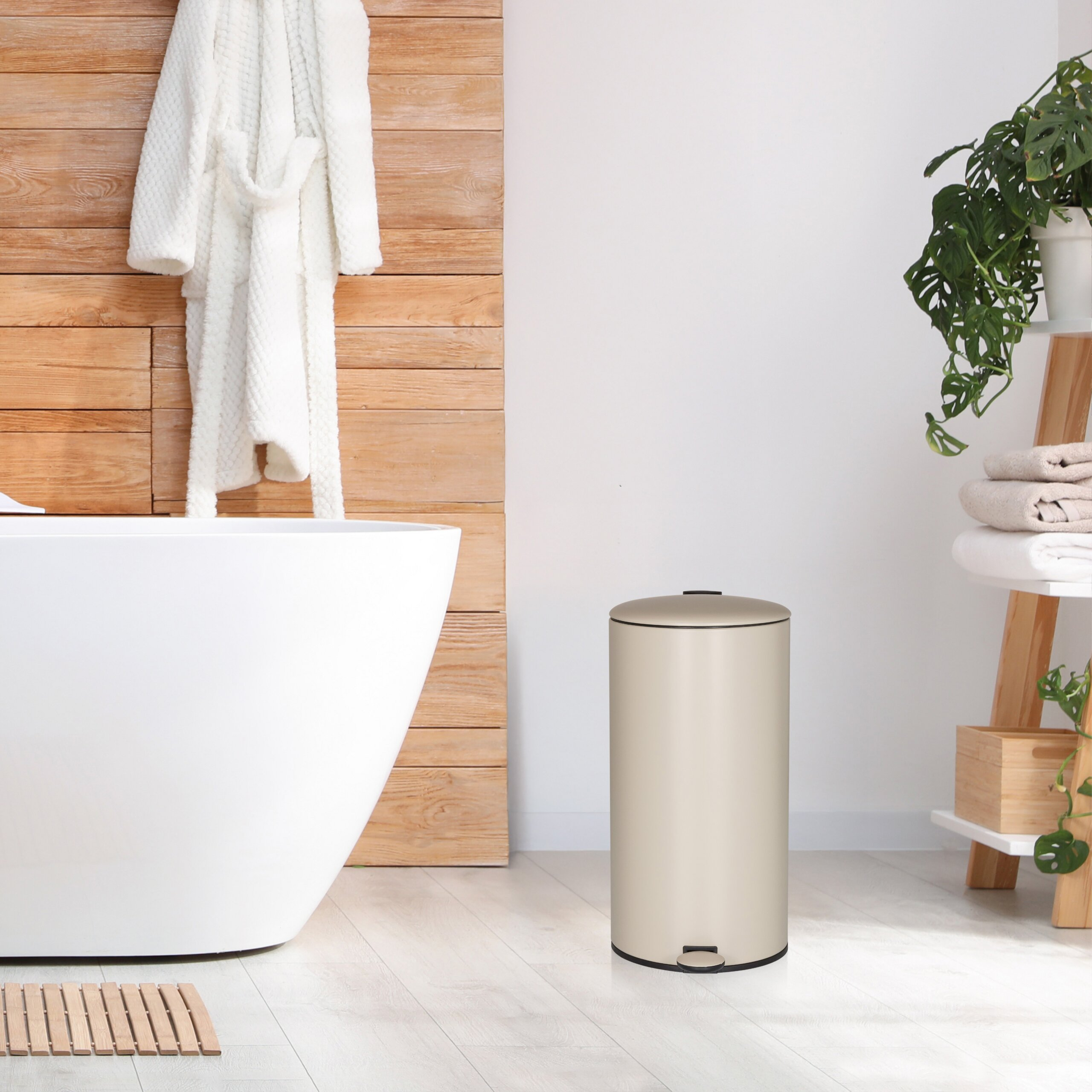 Ein beige Treteimer in einem modernen Bad mit weißer Wanne, Holzwand und Pflanzenregal.