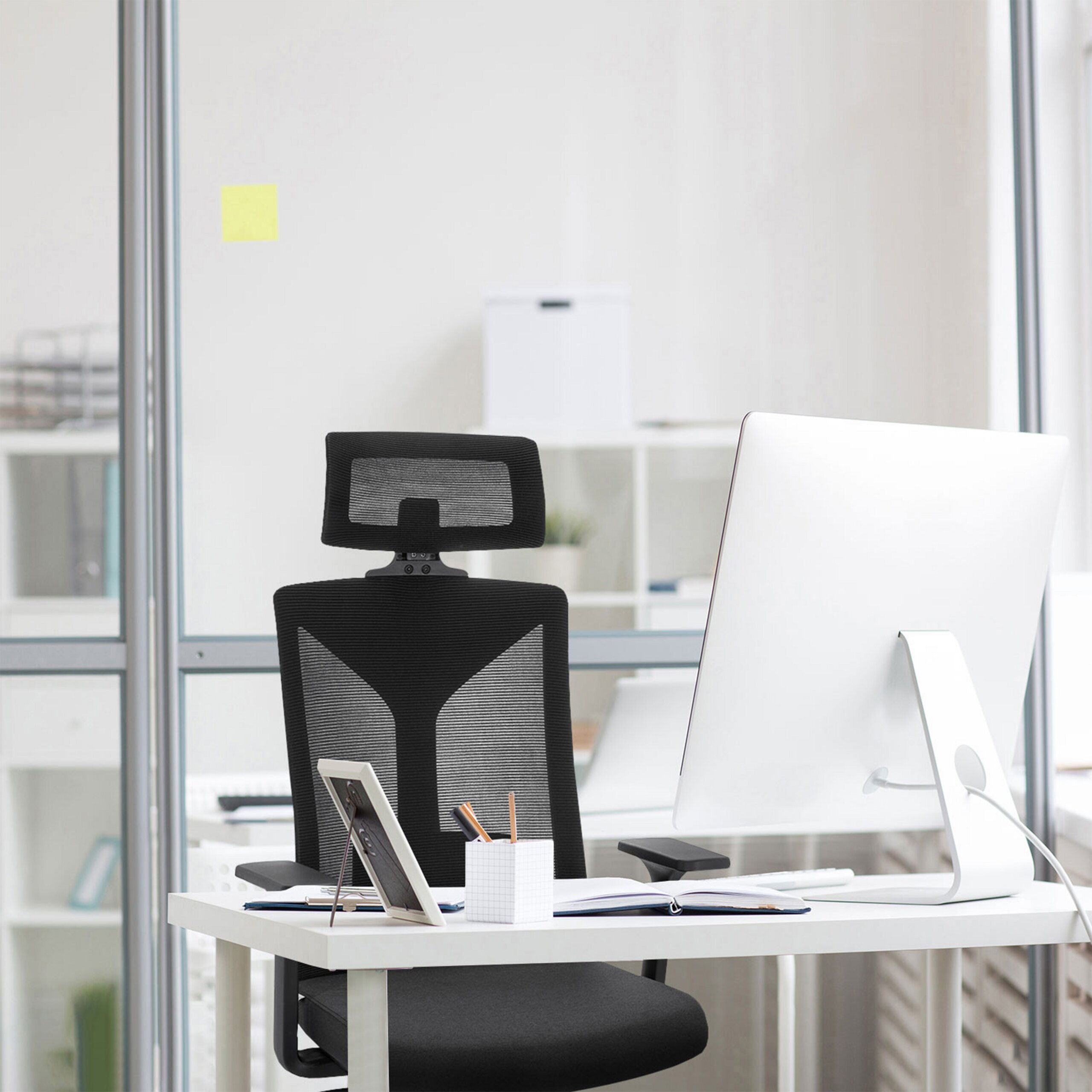 Moderner Arbeitsplatz mit weißem Schreibtisch, schwarzem Bürostuhl und weißem Computer.