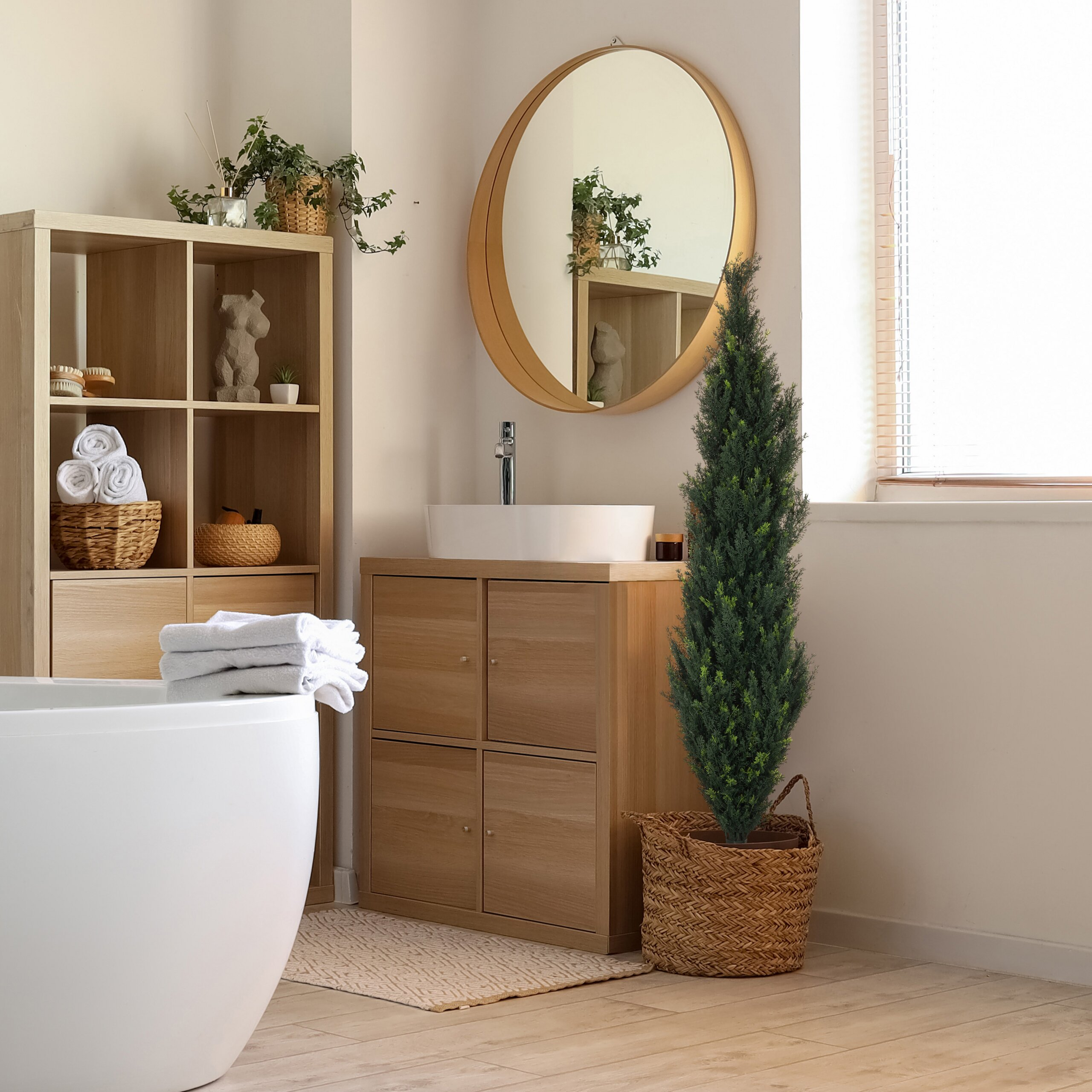 Badezimmer mit Holzmöbeln, runden Spiegel, Badewanne, Waschbecken und grünem Baum in einem Korb.