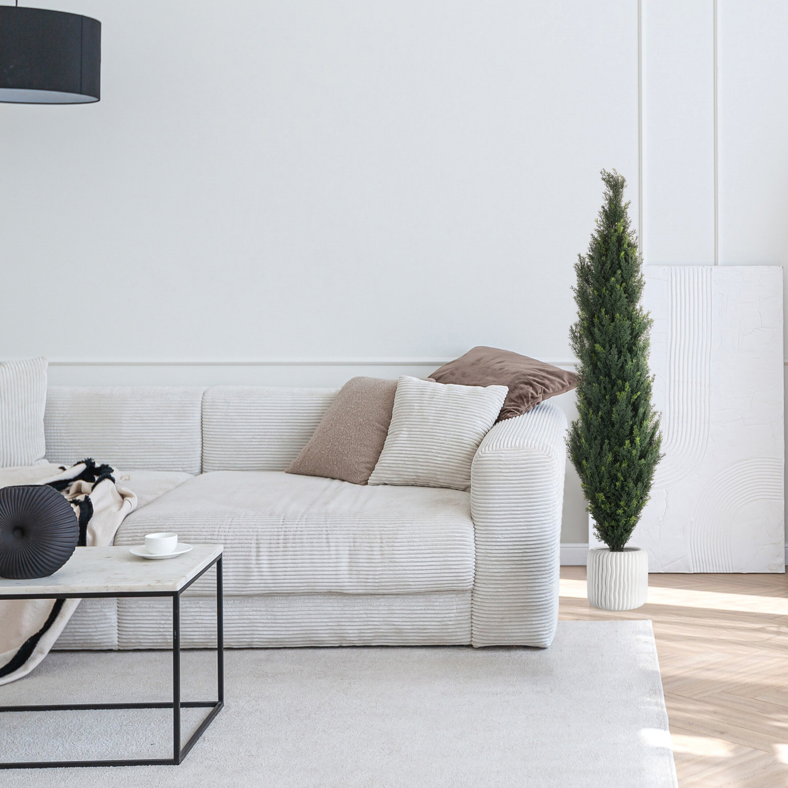 Ein weißes Cordsofa steht in einem hellen Raum mit Couchtisch, Pflanze und Teppich.