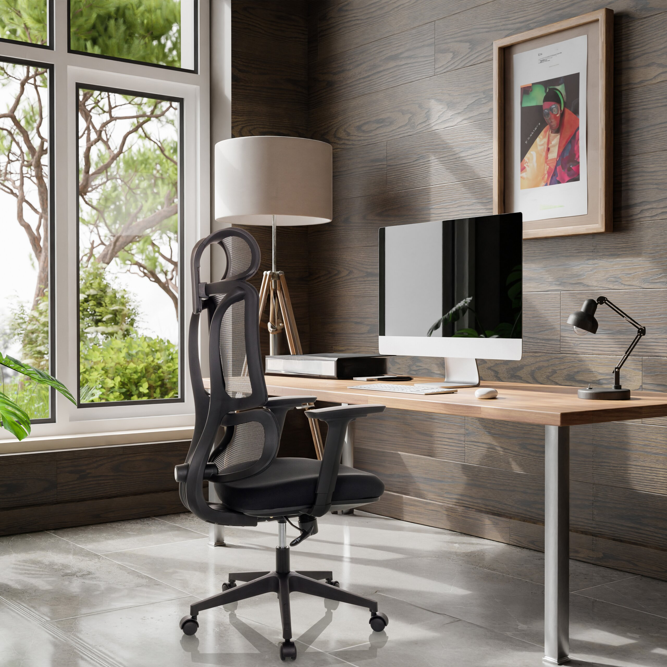Moderne Schreibtisch mit schwarzem Bürostuhl, Computer, Lampe und grossem Fenster mit Blick ins Grüne.
