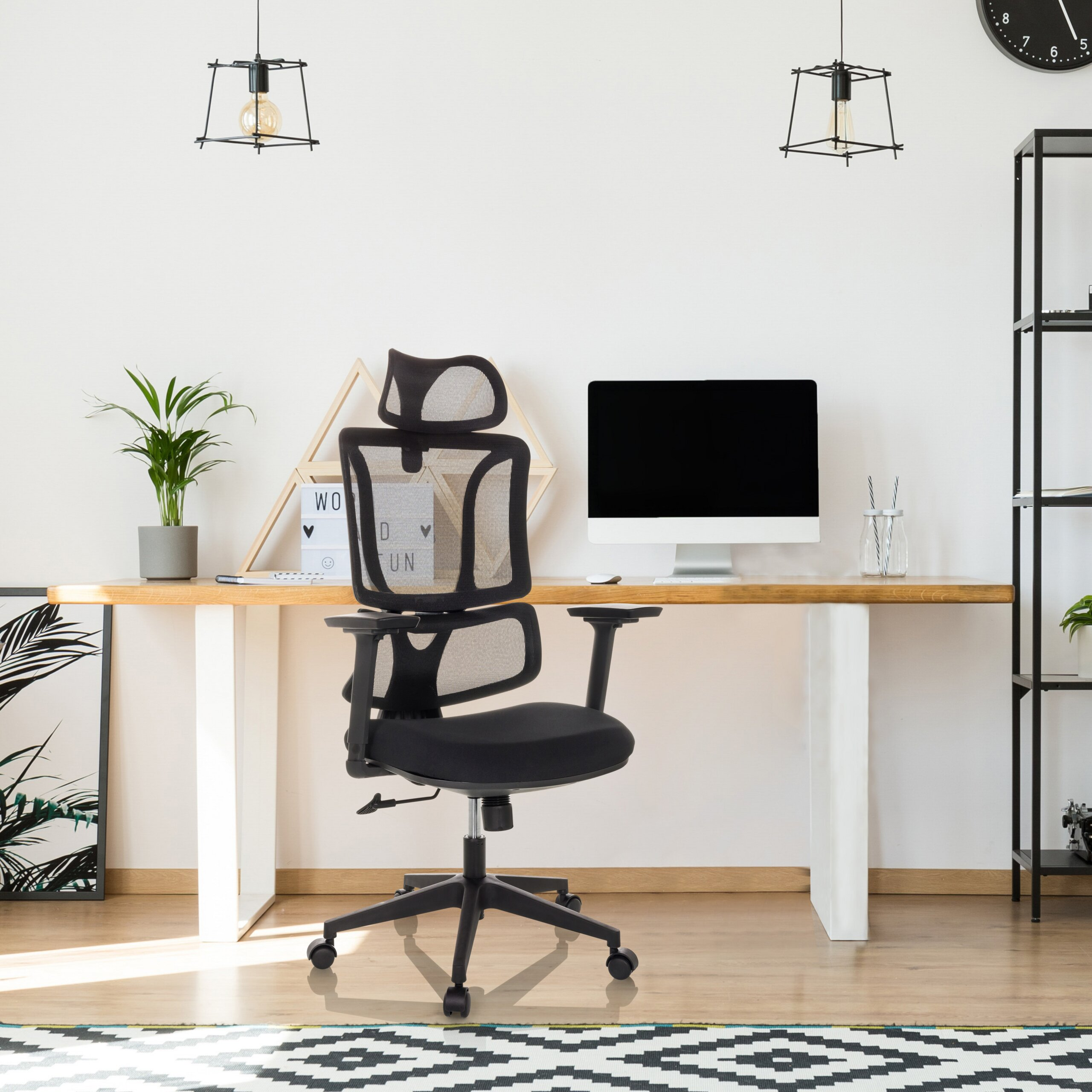 Ein modernes Homeoffice mit schwarzem Netz-Bürostuhl, Holztisch, Computer, Pflanze, Regalen und Hängeleuchten.