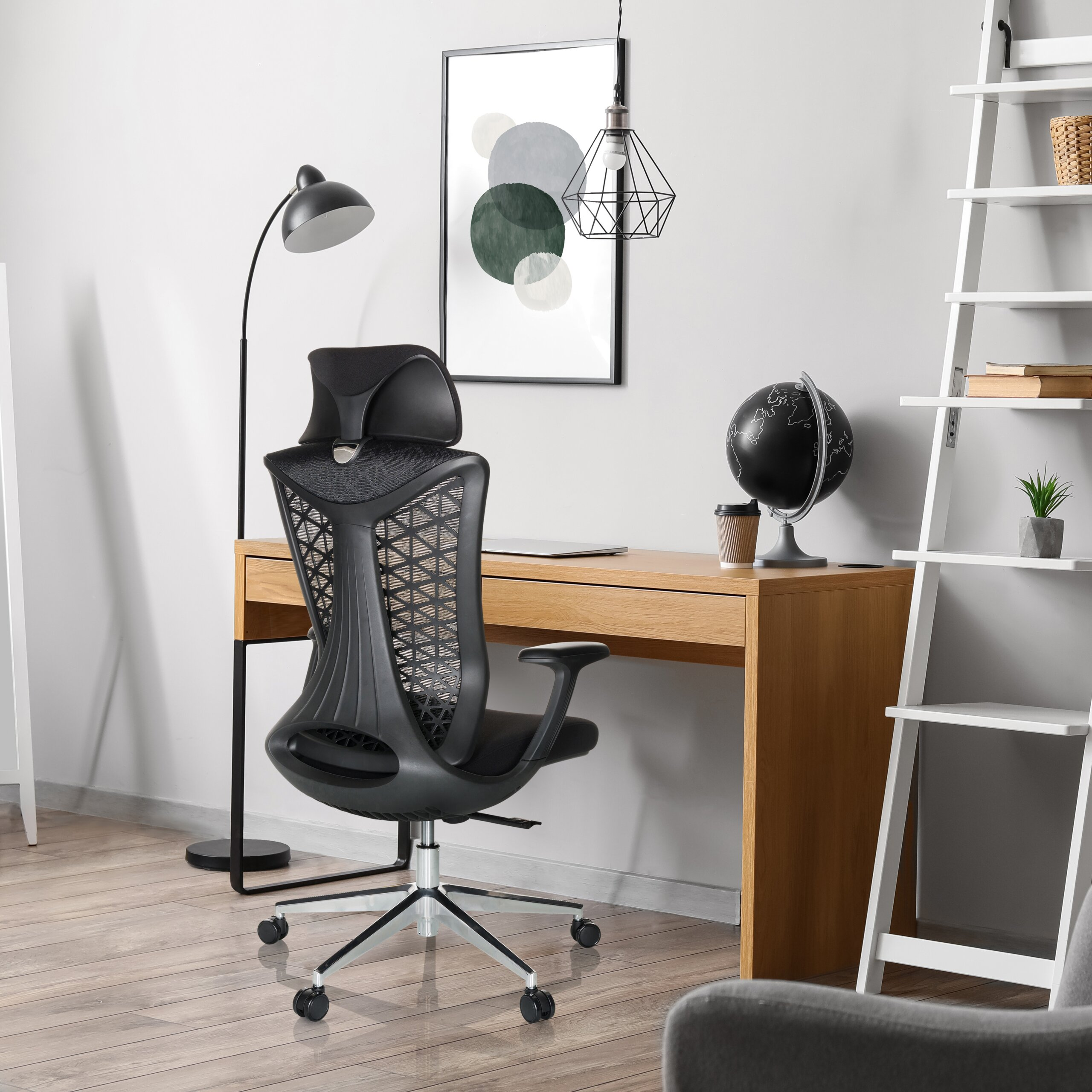 Ein schwarzer, ergonomischer Bürostuhl steht vor einem Holztisch mit Globus, Lampe und weißem Leiterregal.