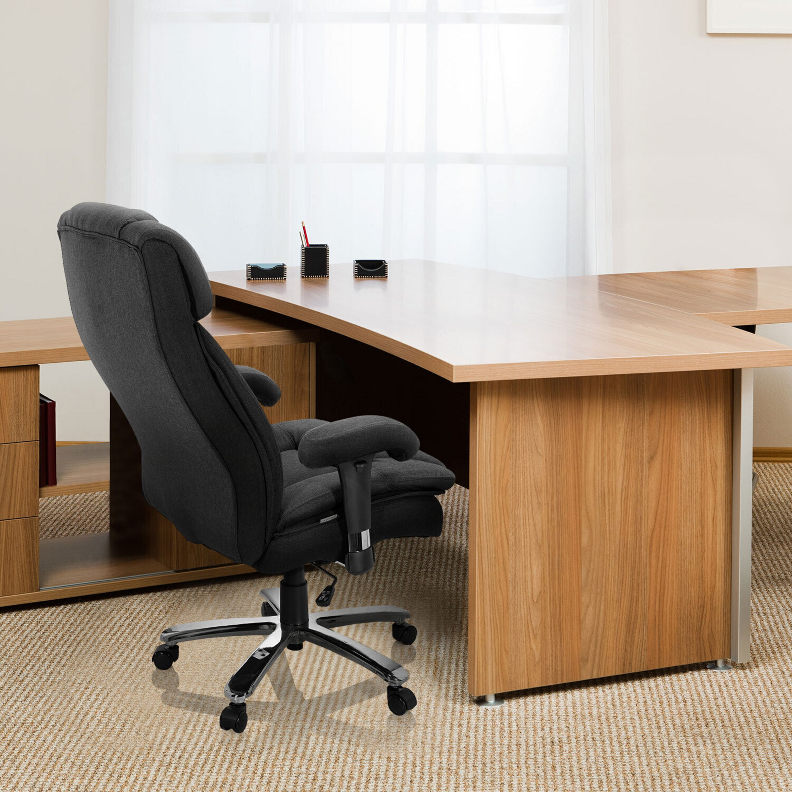 Ein ergonomischer schwarzer Bürostuhl steht vor einem großen Holztisch auf einem beigen Teppich.