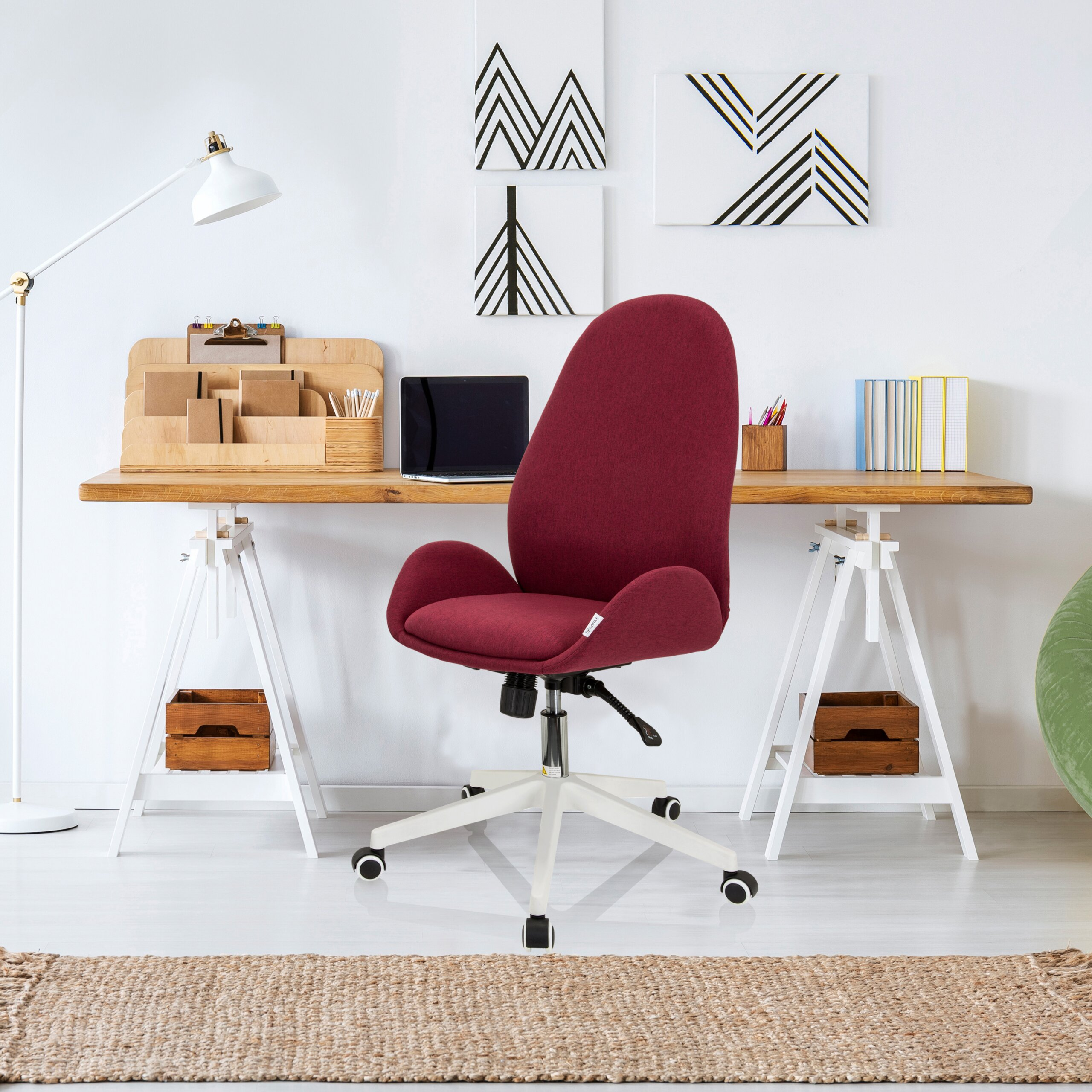 Ein burgunderroter Schreibtischstuhl steht in einem modernen Arbeitszimmer mit Holztisch und weißer Lampe.