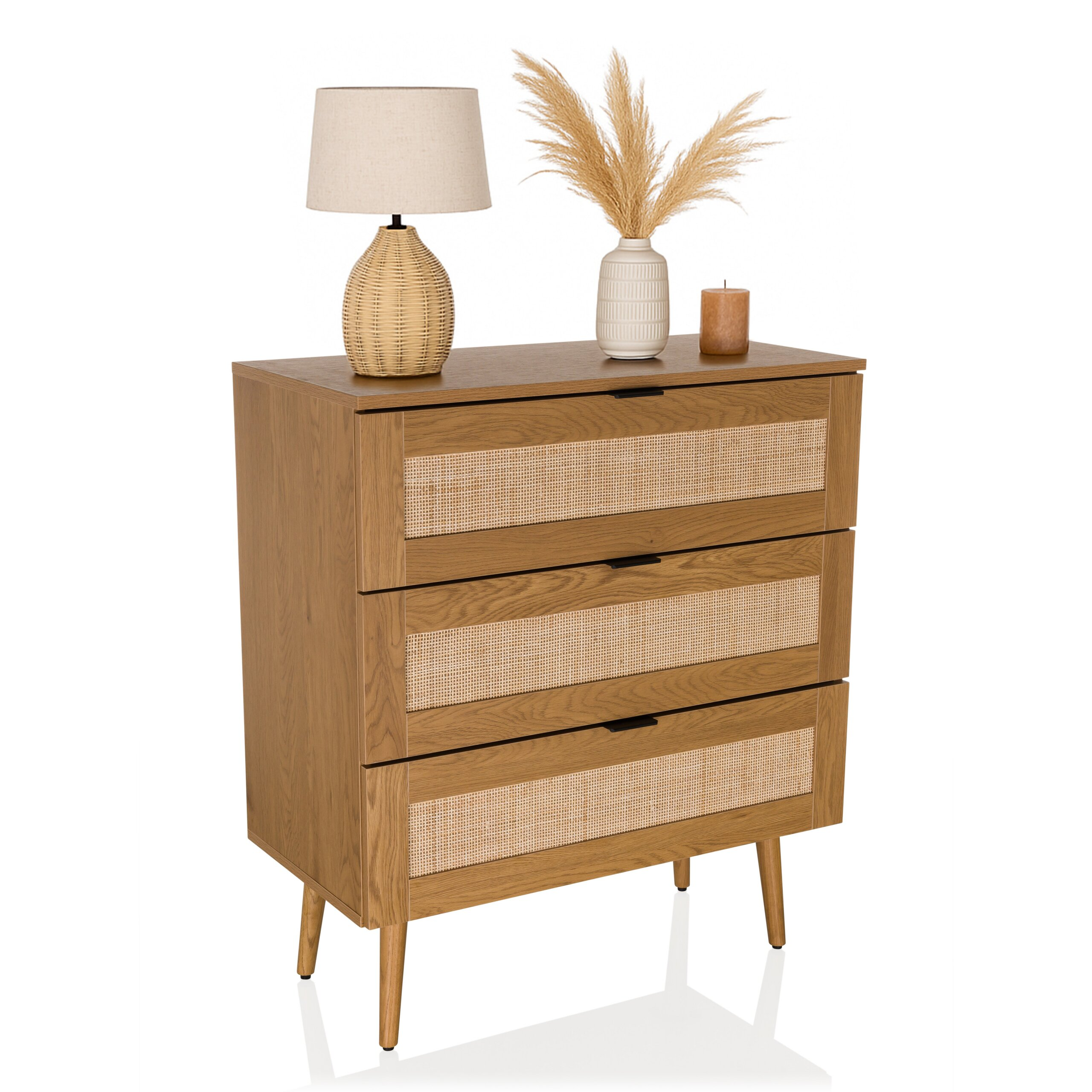 Holzkommode mit drei Rattan-Schubladen, darauf stehen Lampe, Vase mit Gras und Kerze.