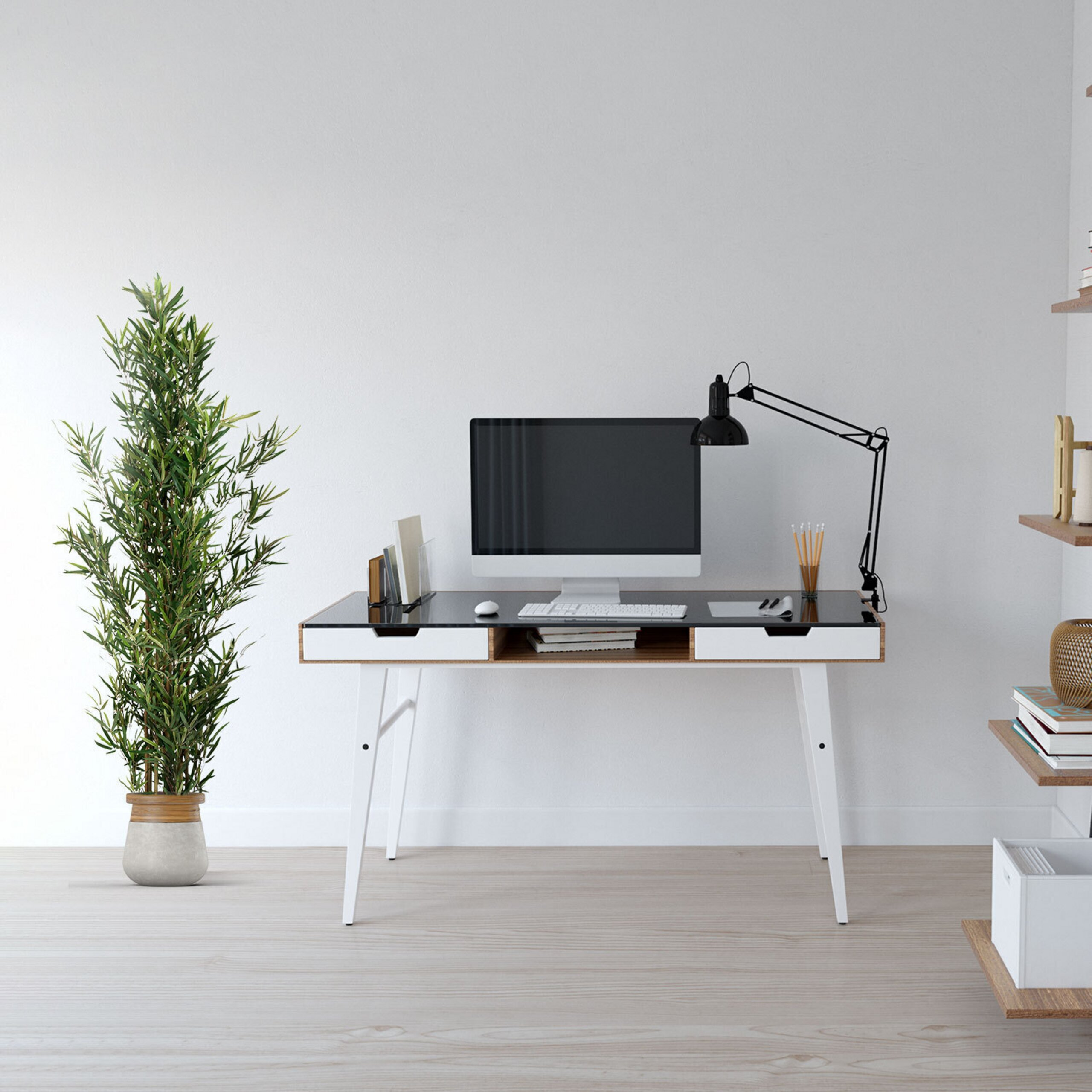 Ein moderner Schreibtisch mit Computer, Lampe und Büchern steht an einer weißen Wand neben einer Topfpflanze.