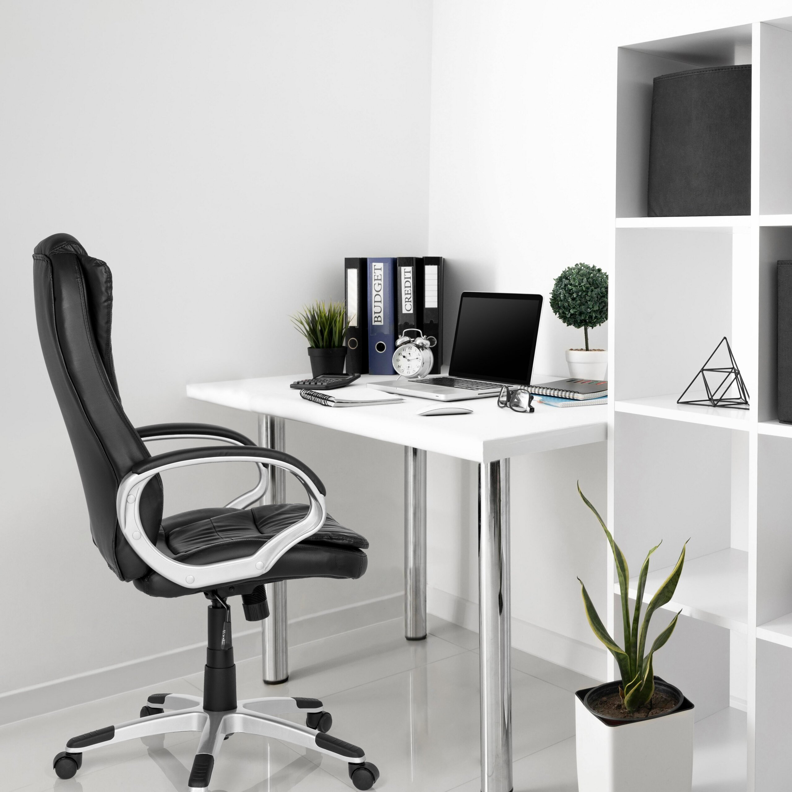 Moderne Büro-Ecke mit Schreibtisch, schwarzem Drehstuhl, Laptop, Ordnern, Pflanzen und weißem Regal.
