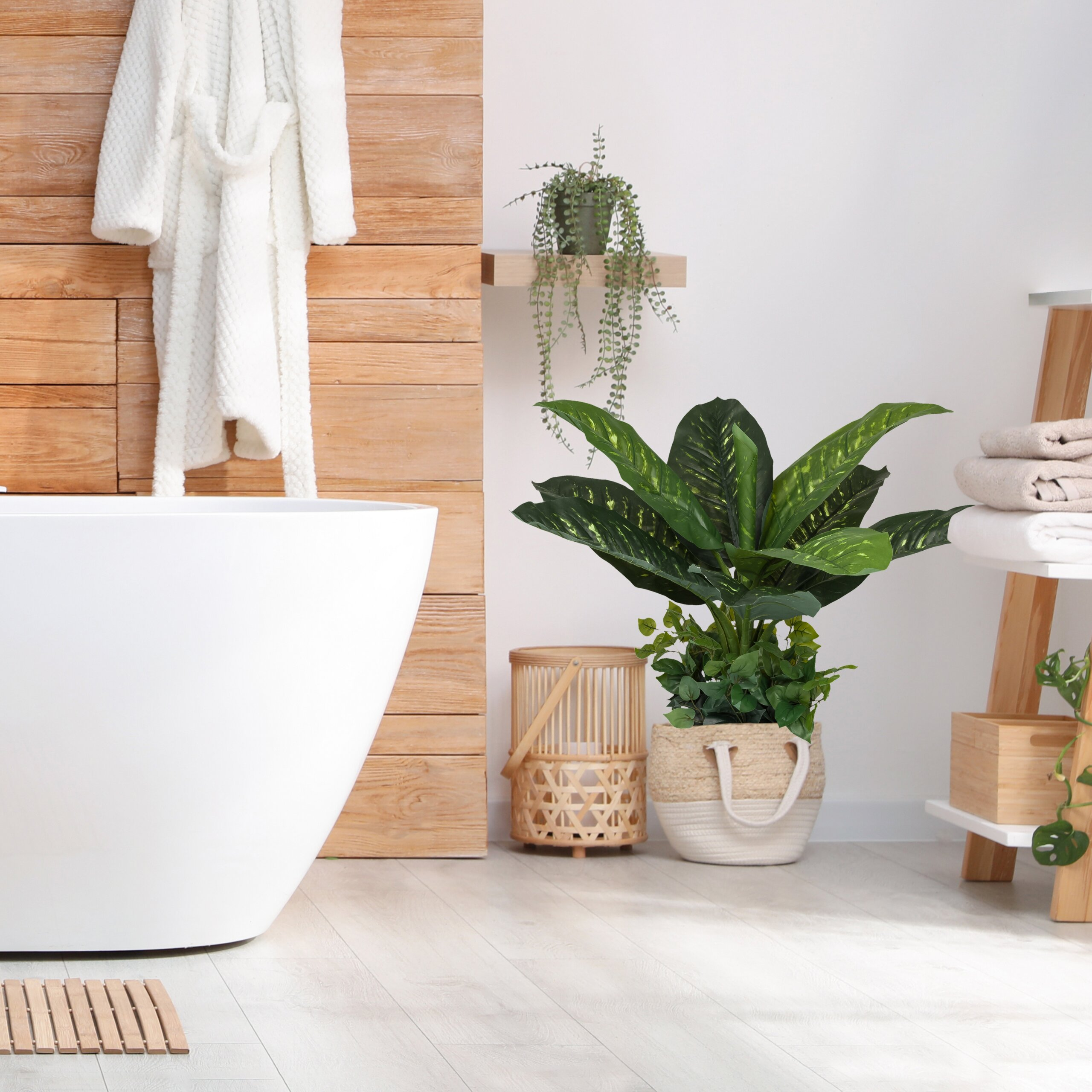 Modernes Badezimmer mit weißer Wanne, Holzwand, Bademantel, großen grünen Pflanzen und Handtuchleiter.