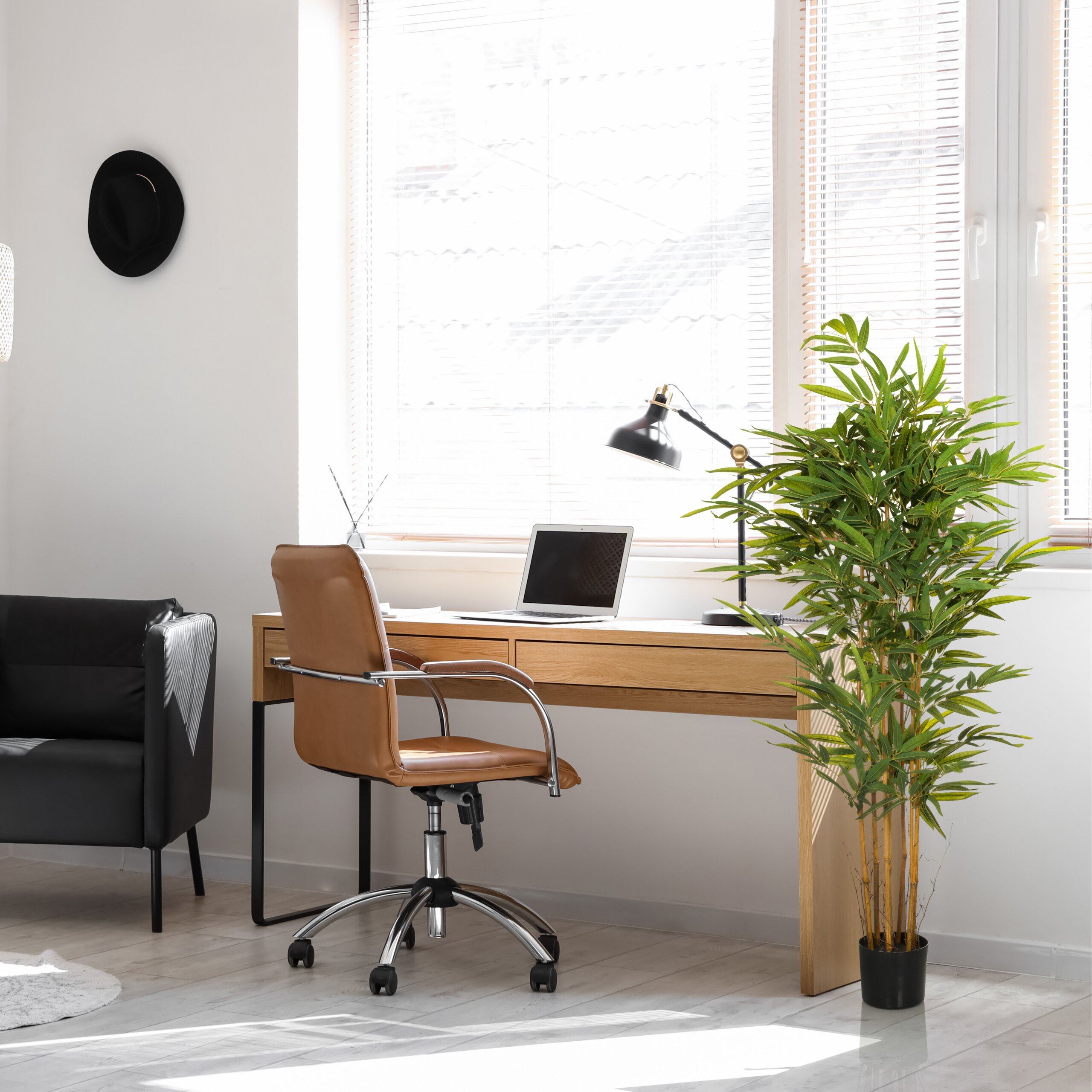 Helles modernes Büro mit Holztisch, Laptop, braunem Stuhl, Lampe, Topfpflanze und schwarzem Sessel.