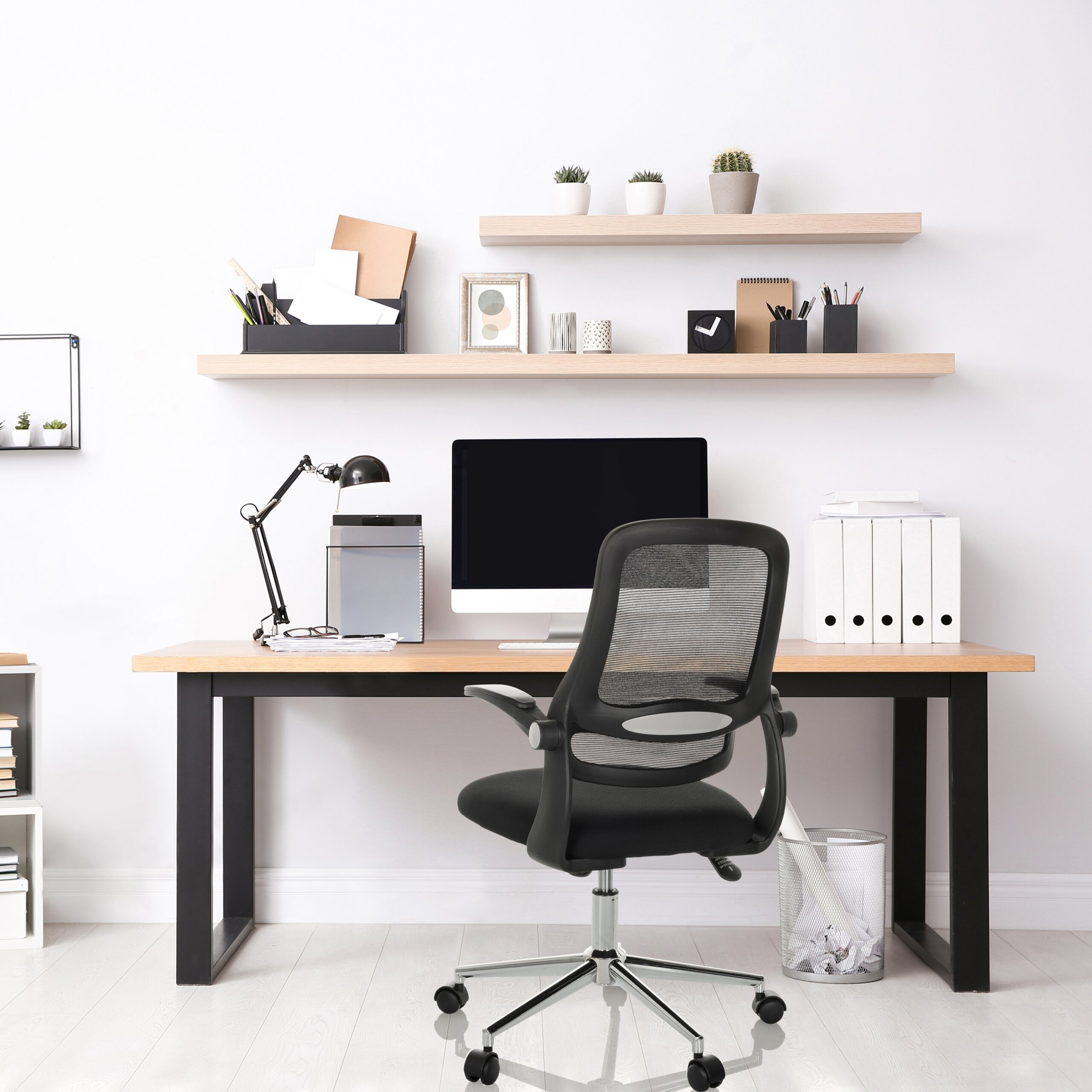 Ein modernes Homeoffice mit Schreibtisch, Computer, schwarzem Mesh-Bürostuhl und Holzregalen mit Pflanzen und Dekor.