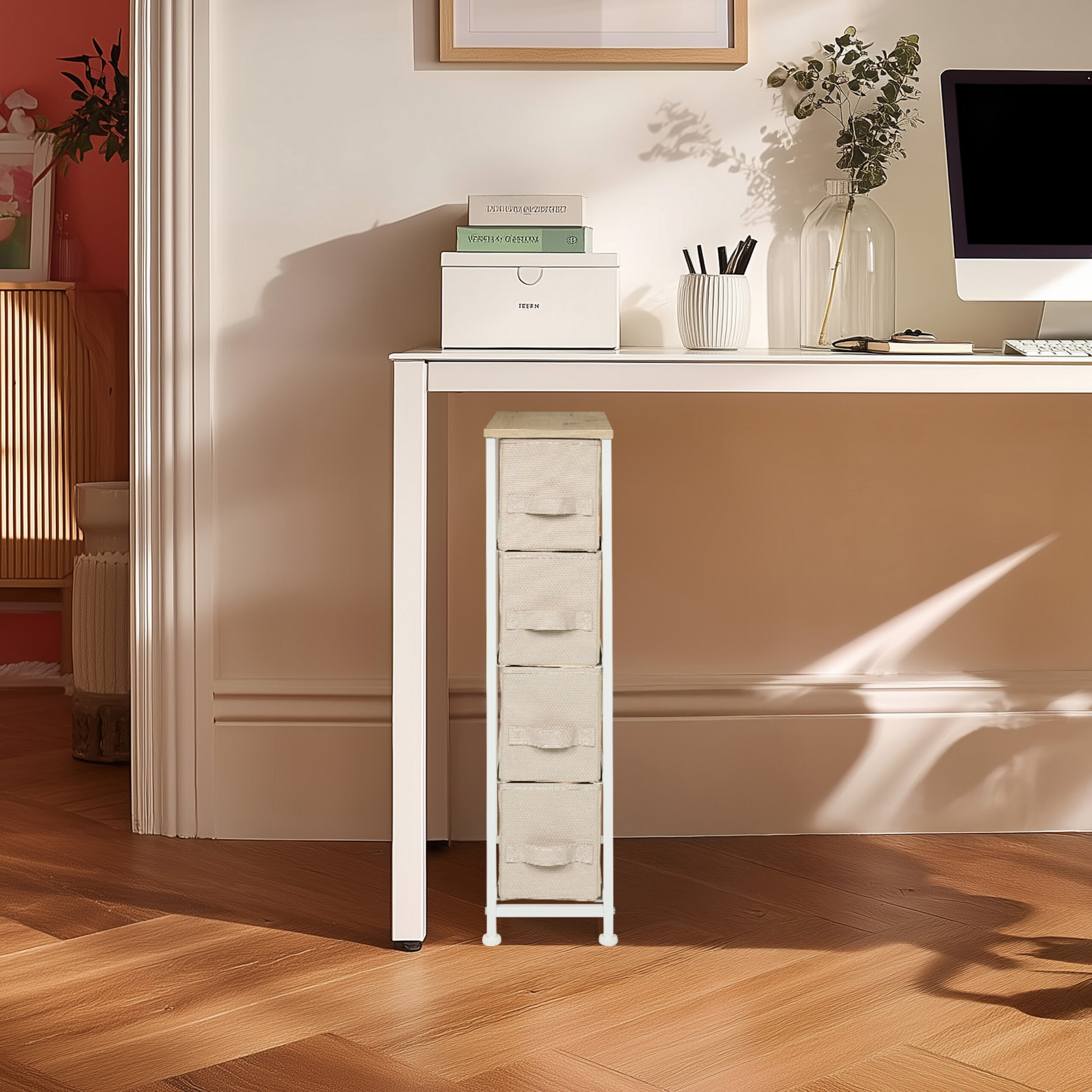 Ein schmaler, weißer Schrank mit vier beigen Stoffschubladen steht unter einem weißen Schreibtisch mit Computer.