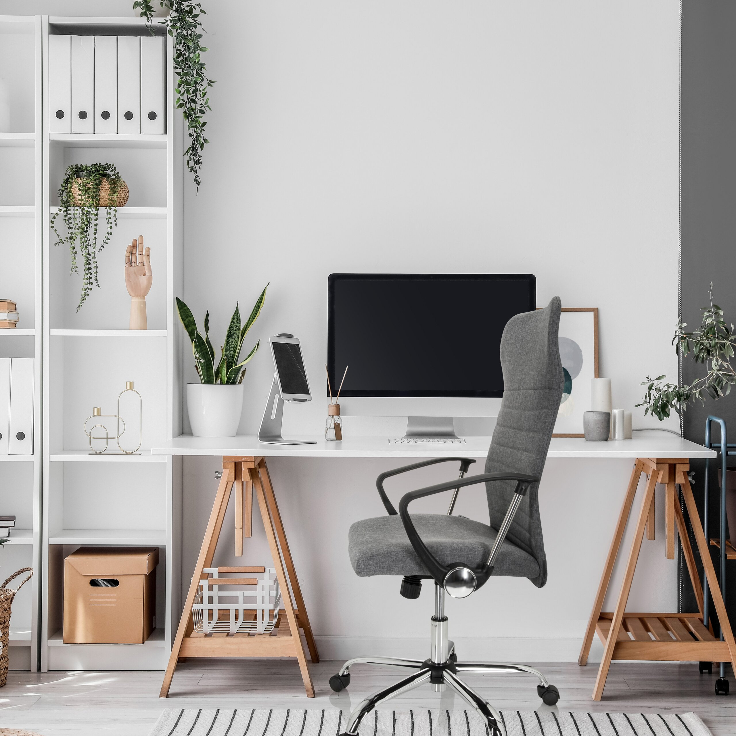 Moderne Arbeitsplatz mit weißem Schreibtisch, grauem Stuhl, Computer und Regale voller Pflanzen.