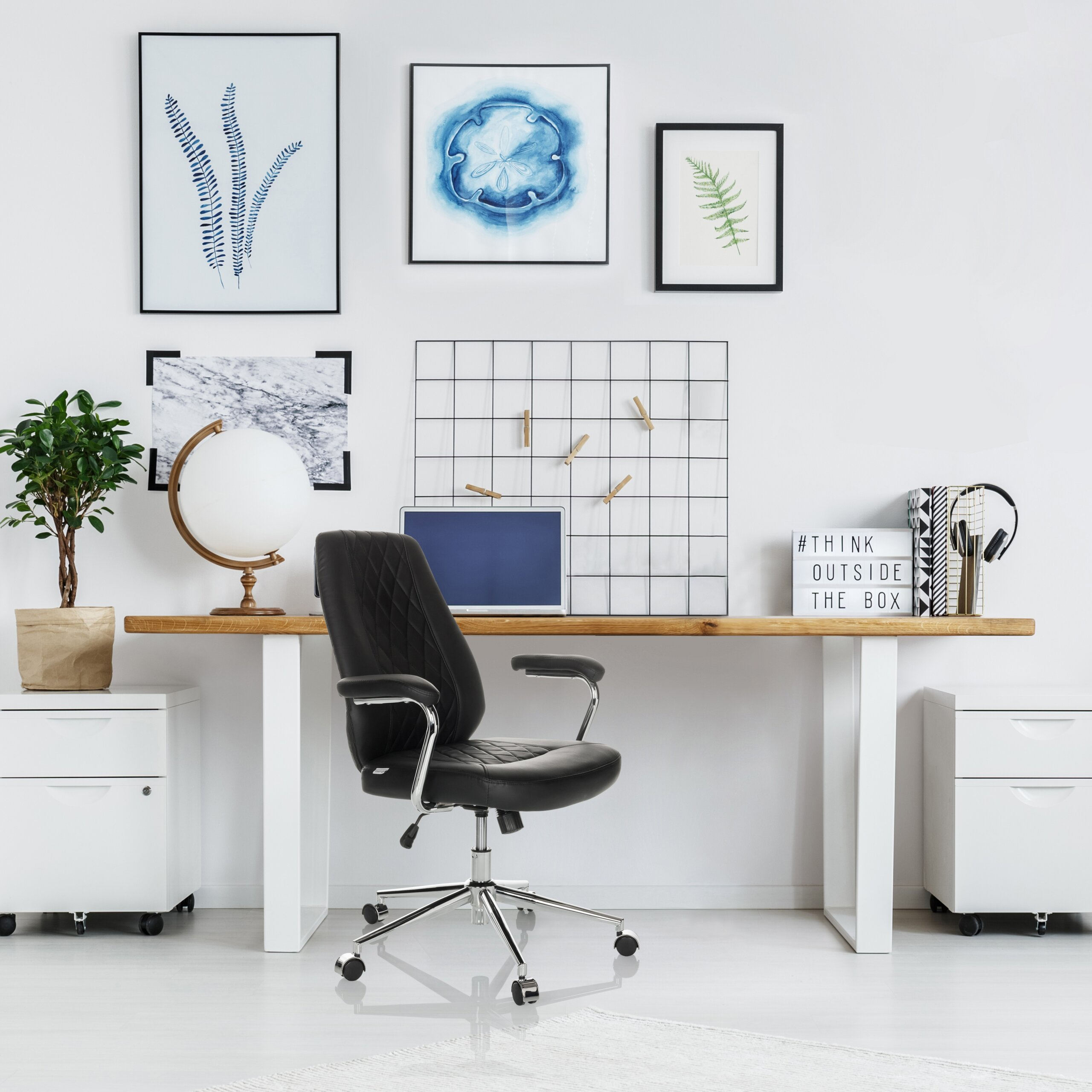 Moderne Schreibtischecke mit schwarzem Drehstuhl, Laptop, Globus, Pflanzen und gerahmten Bildern an weißer Wand.