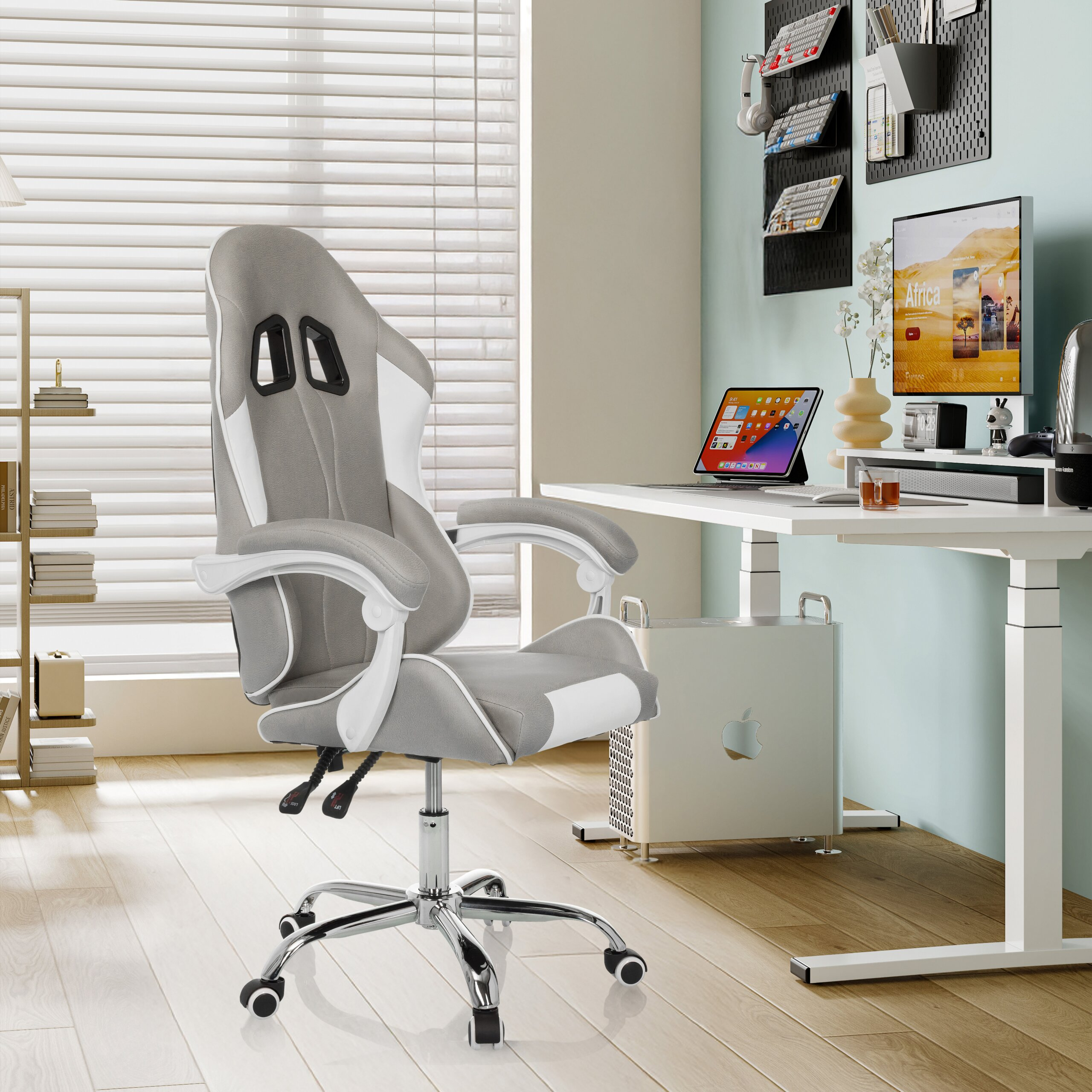Ein grauer und weißer ergonomischer Gaming-Stuhl in einem modernen Arbeitszimmer mit Computertisch und Jalousien.