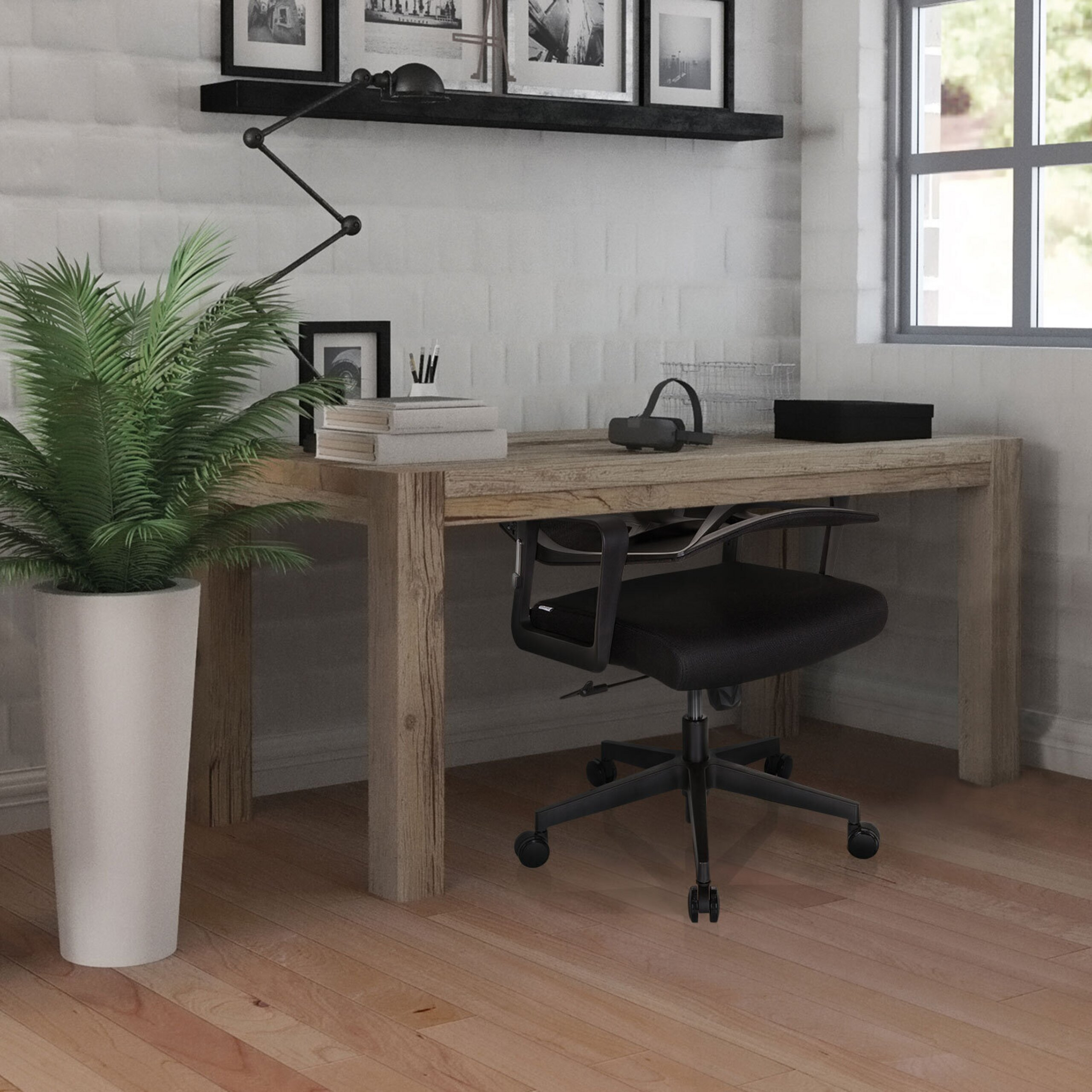 Ein heller Arbeitsbereich mit Holztisch, schwarzem Drehstuhl, großer Pflanze im weißen Topf und gerahmten Bildern.