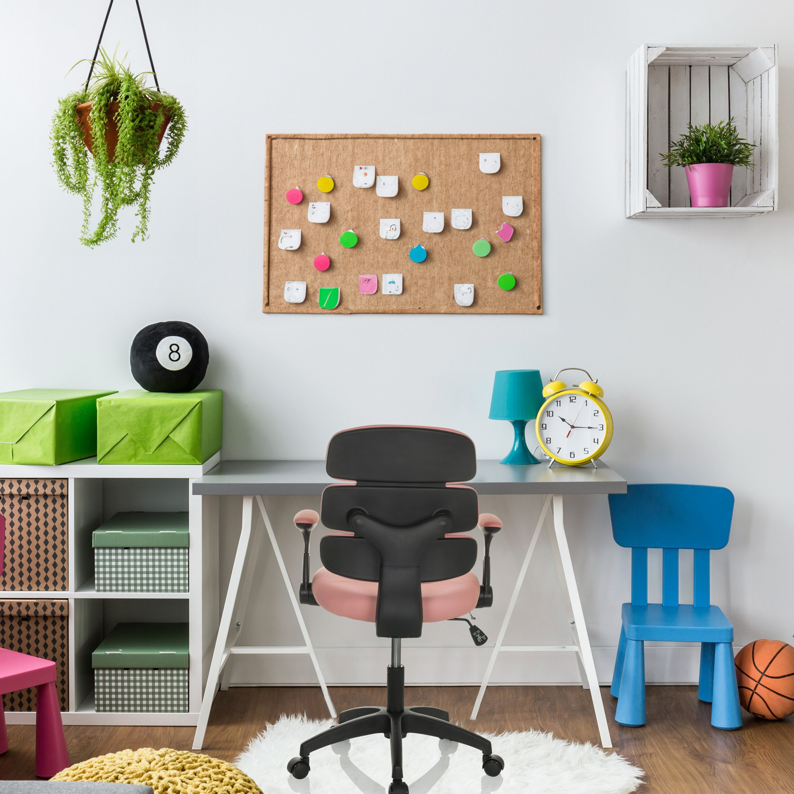 Ein buntes Arbeitszimmer mit Schreibtisch, rosa Bürostuhl, Pinnwand, Aufbewahrungsboxen und Wanddeko.