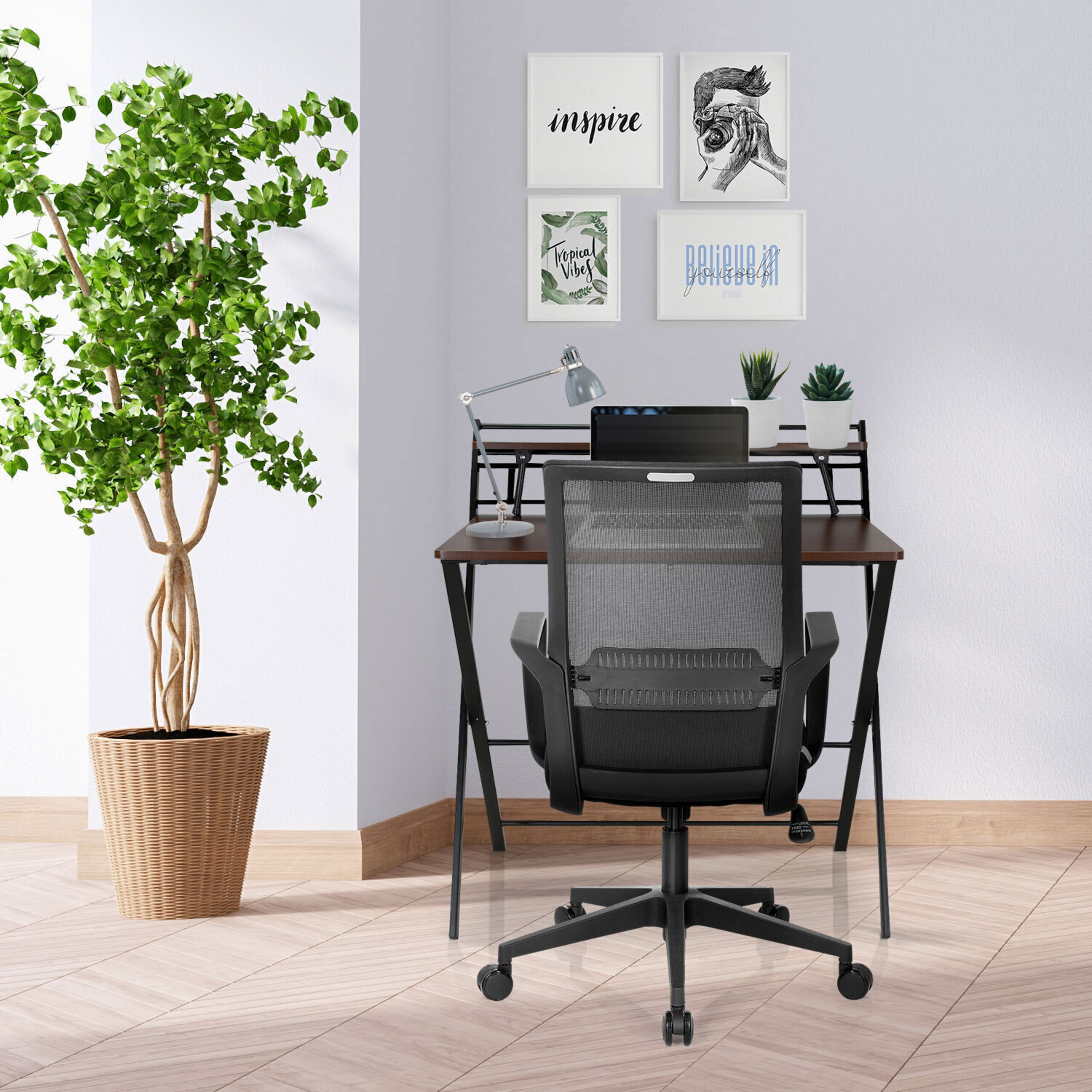 Ein Heimbüro-Ecke mit Holztisch, schwarzem Netzstuhl, Laptop, Schreibtischlampe, Wandkunst und großer Pflanze.