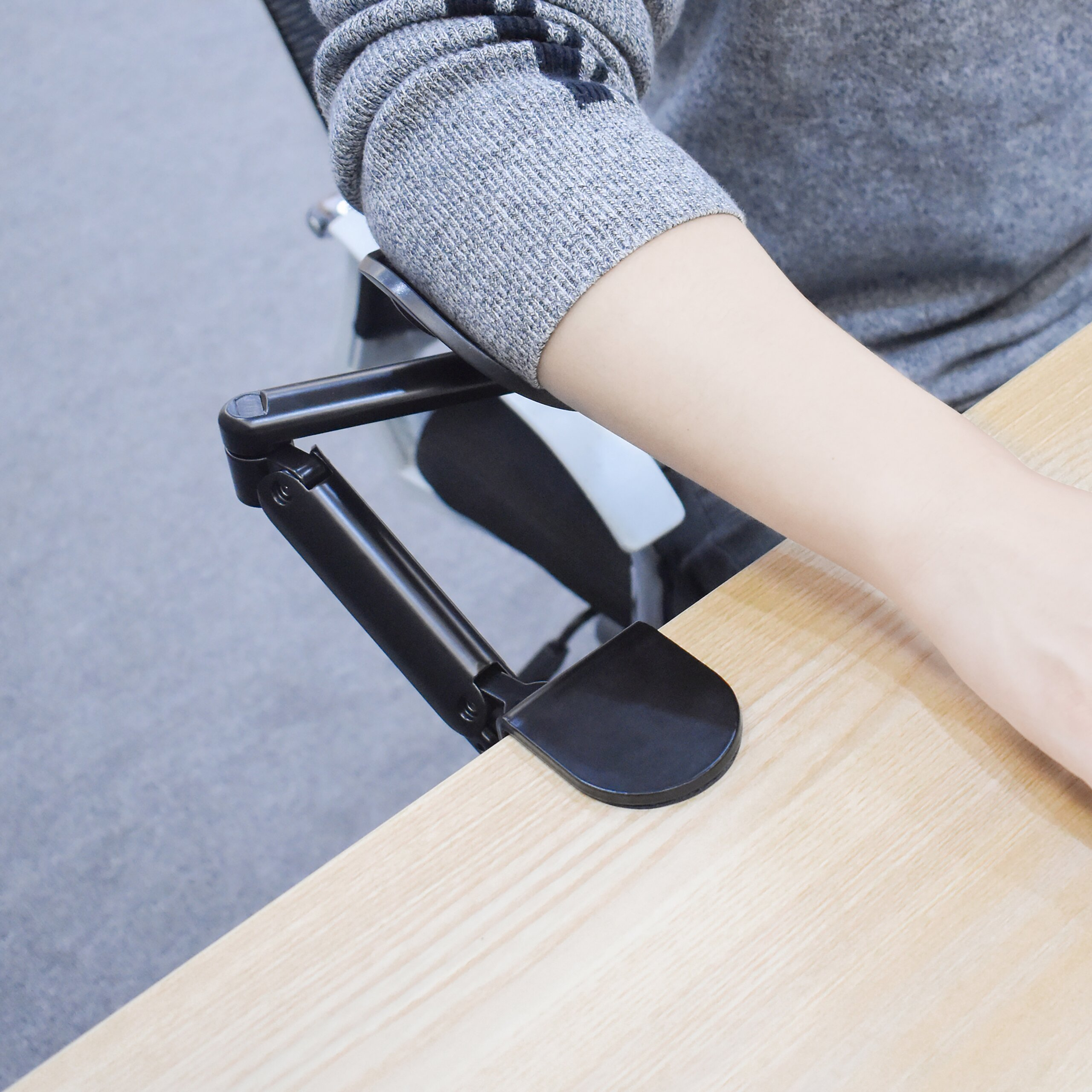 Eine Person ruht ihren Arm auf einer ergonomischen schwarzen Armlehne an einem Holzschreibtisch.