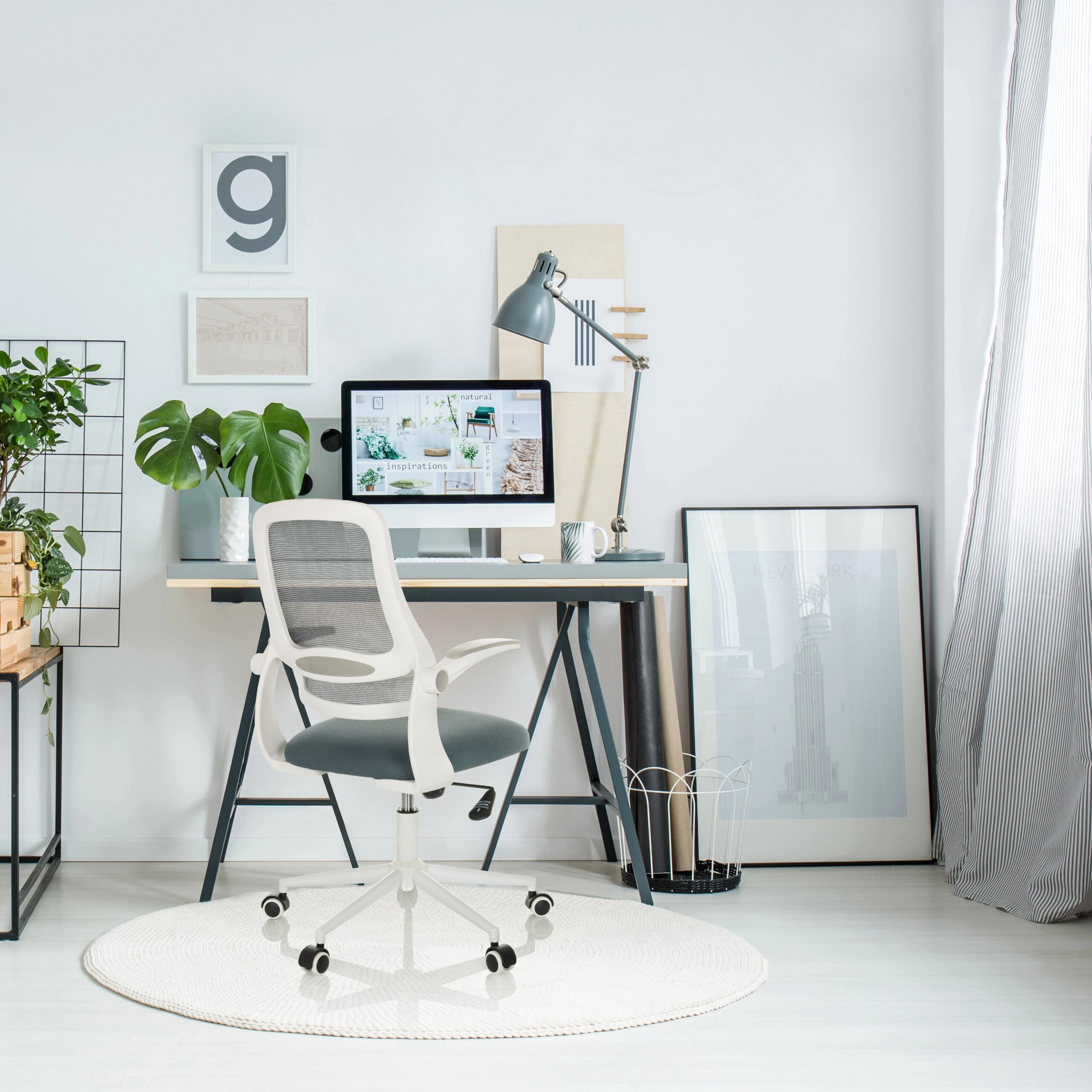 Ein modernes Homeoffice mit weiß-grauem Schreibtischstuhl, Computer, Lampe, Pflanzen und Kunst an weißen Wänden.