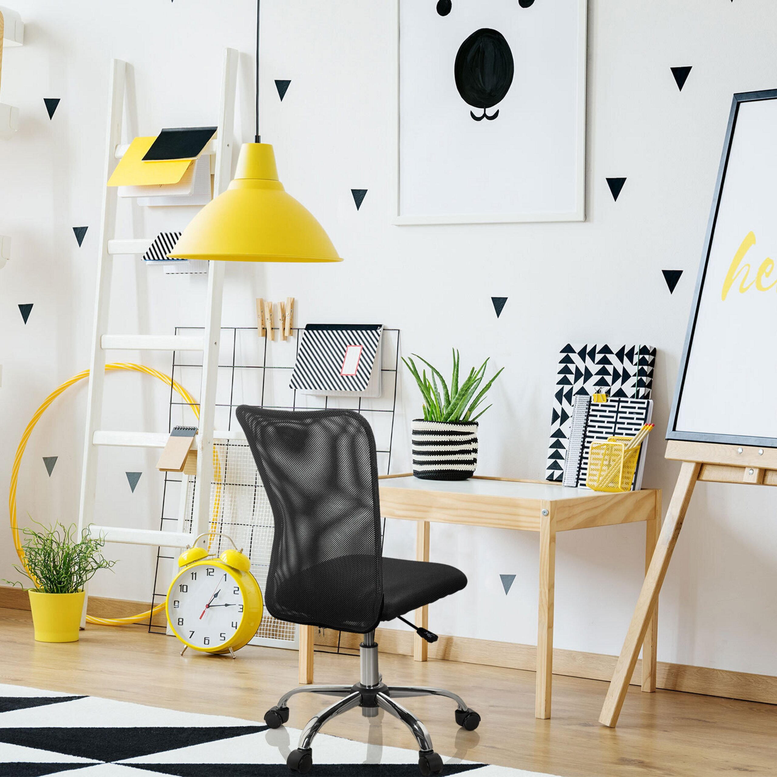 Ein helles Arbeitszimmer mit schwarzem Bürostuhl, gelber Lampe und Wanddeko.