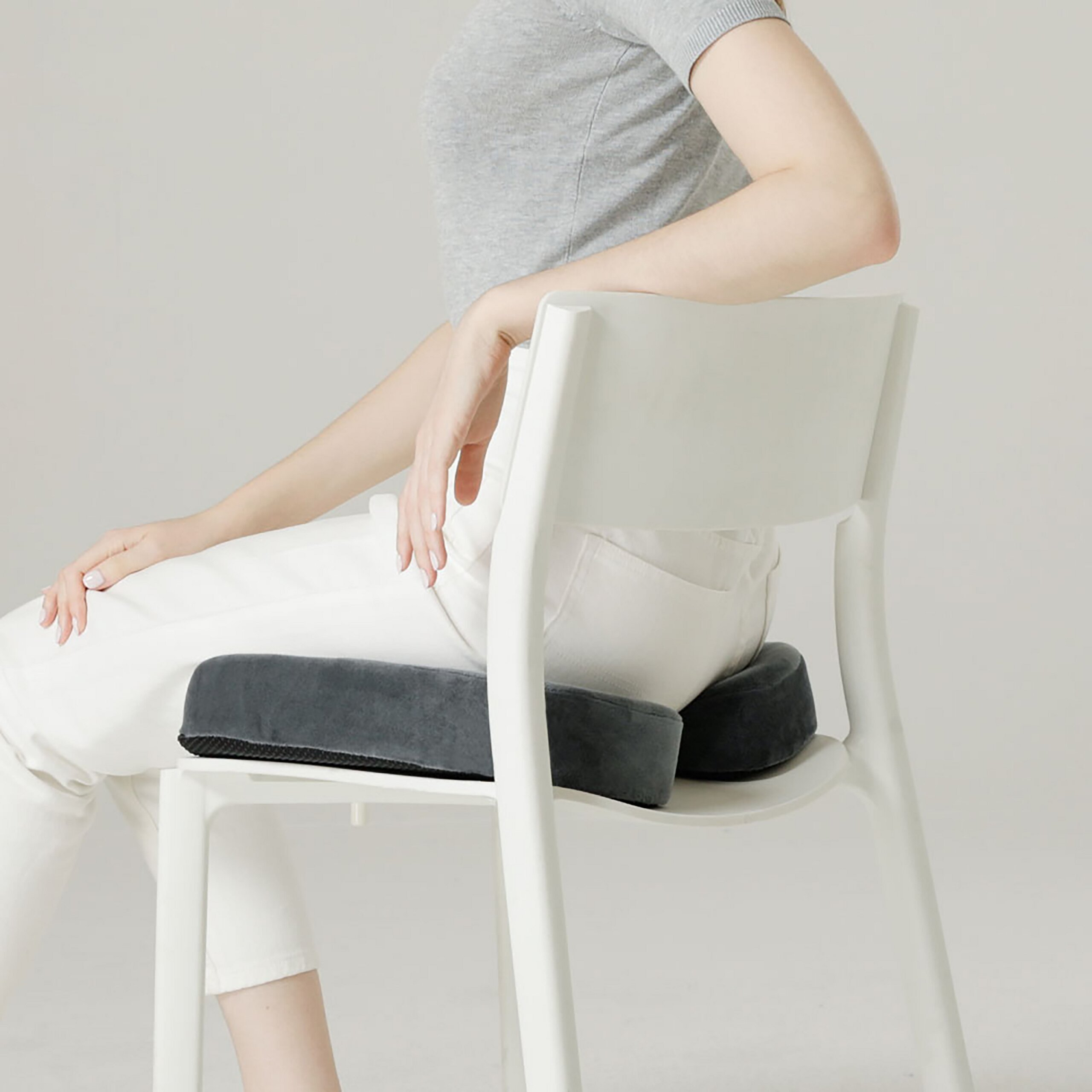 Eine Person sitzt auf einem weißen Stuhl mit grauen ergonomischen Kissen.