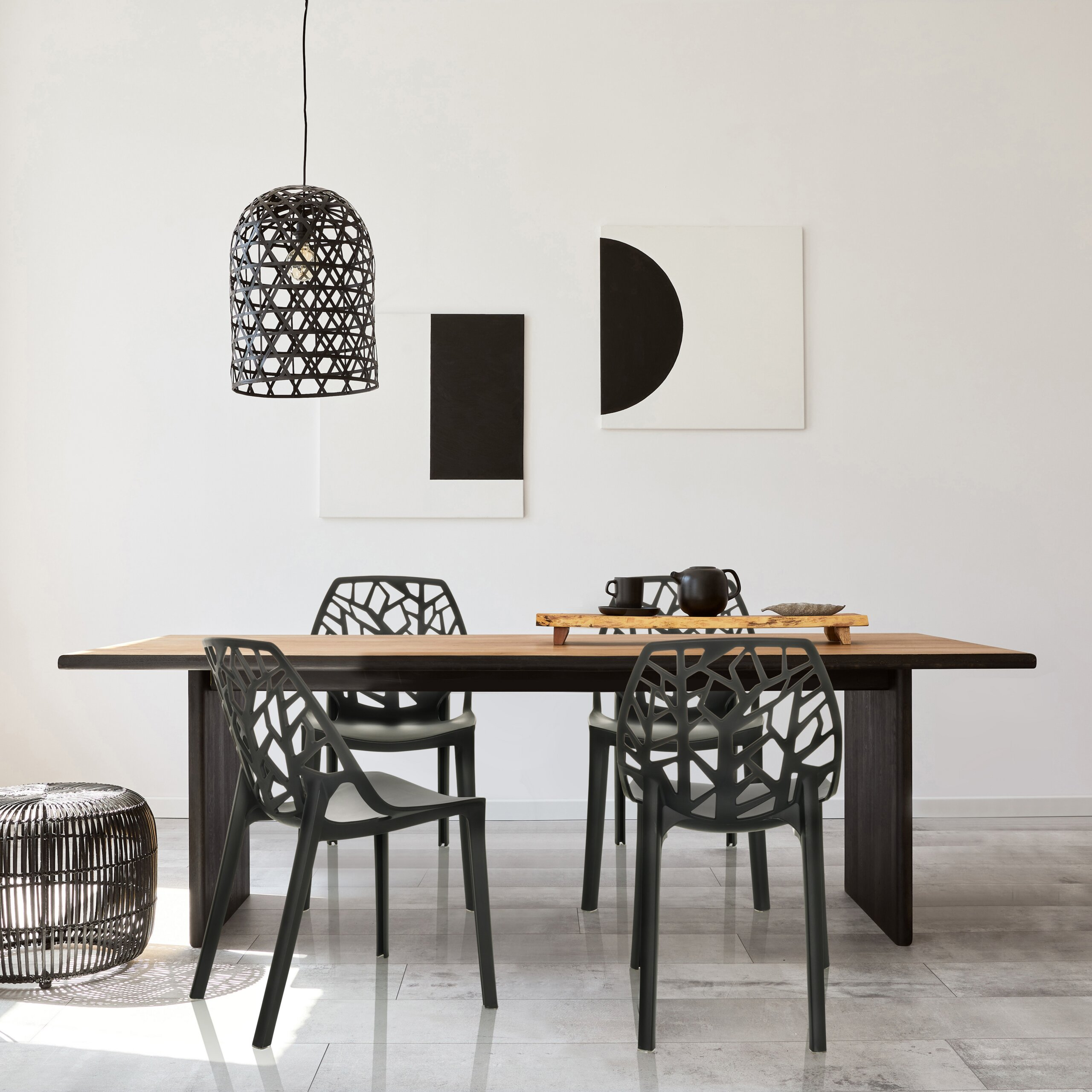 Moderne Essecke mit Holztisch, schwarzen Netzstühlen, Hängeleuchte und abstrakter Kunst an weißer Wand.