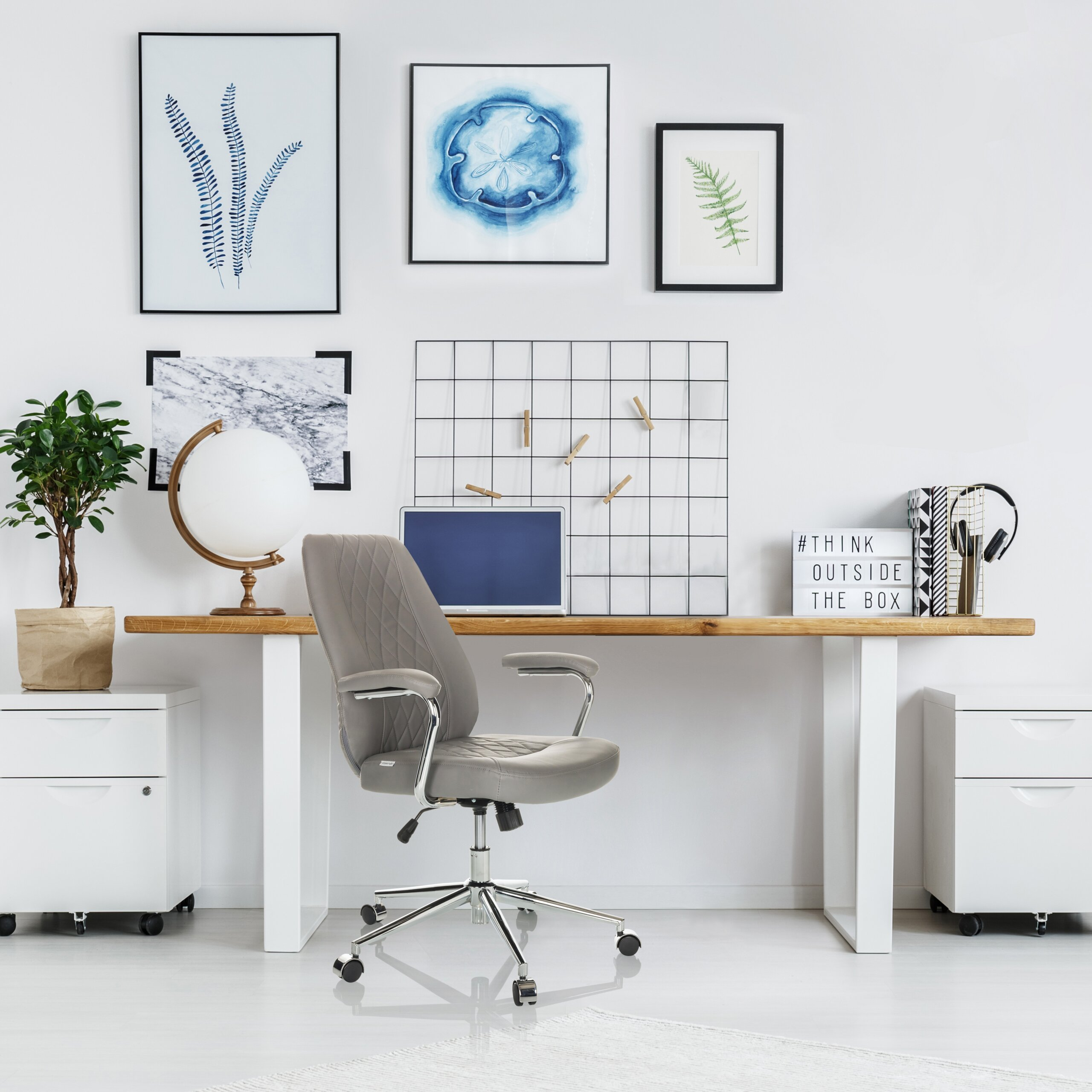 Moderner Arbeitsplatz mit grauem Bürostuhl, Holztisch, Laptop, Globus, Wandkunst und Pflanzen in hellem Zimmer.