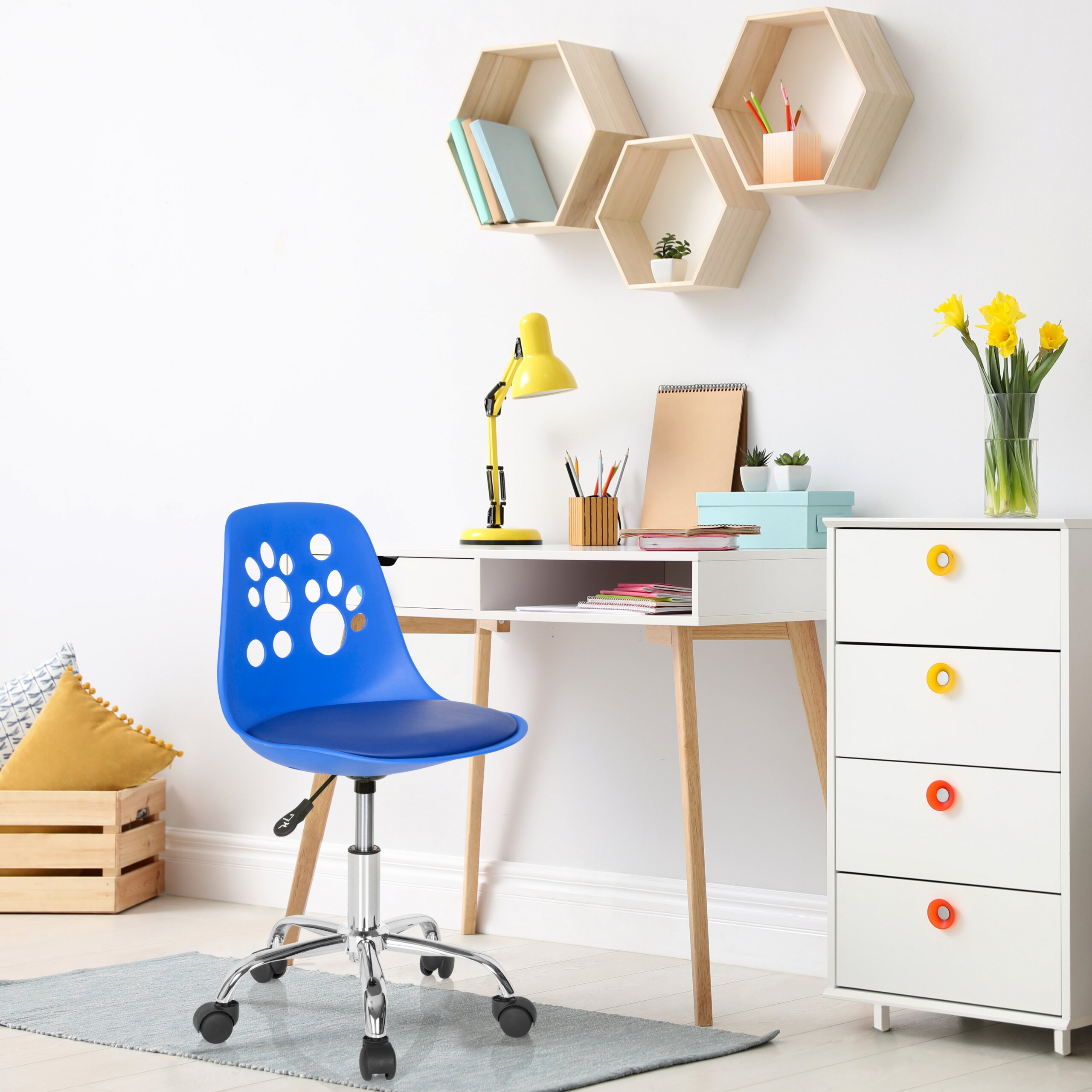 Ein Kinderzimmer mit blauem Stuhl, weißem Schreibtisch, gelber Lampe, hexagonalen Regalen und einer Kommode.