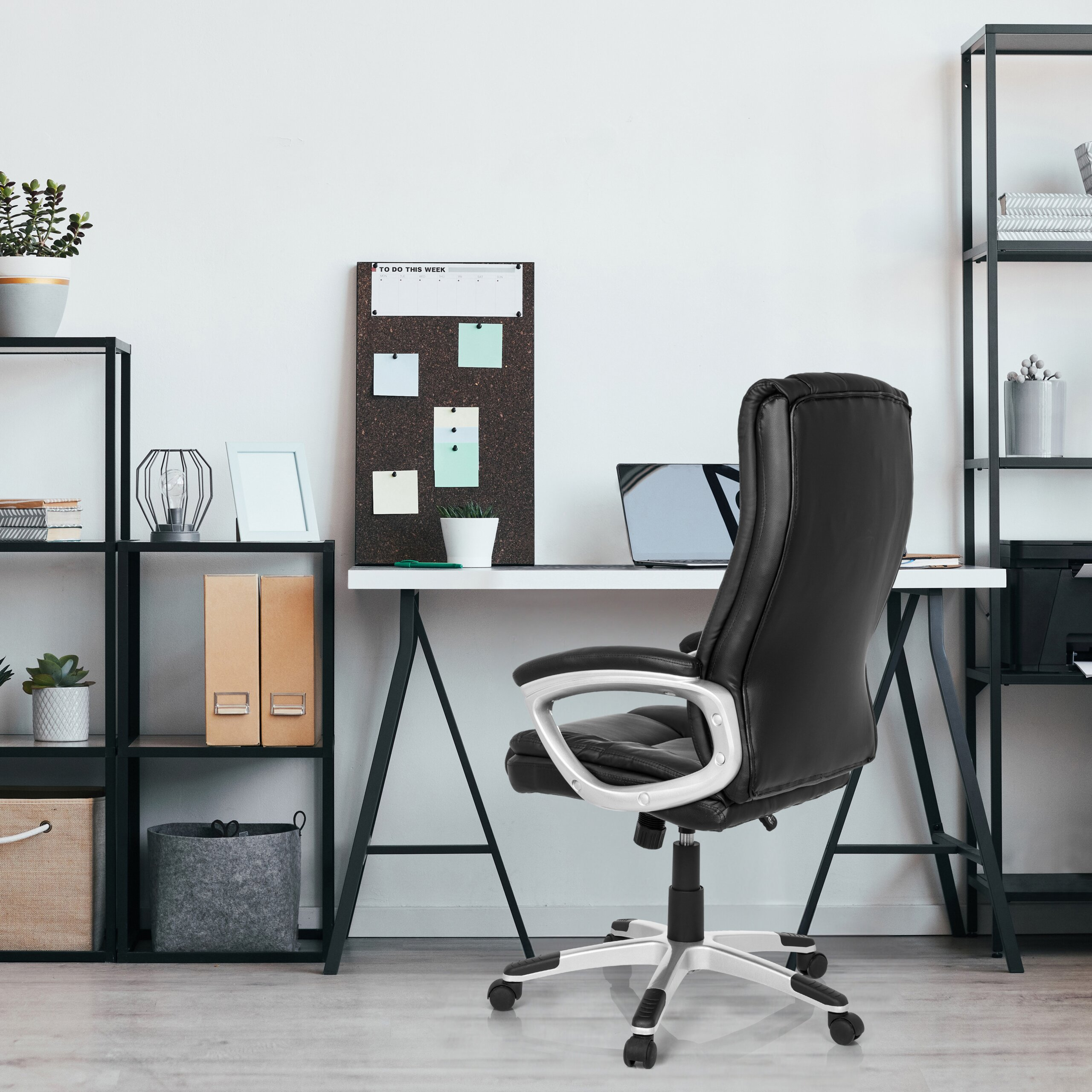 Ein Heimbüro mit schwarzem Ledersessel, weißem Schreibtisch, Laptop, Pinnwand und schwarzen Metallregalen an den Seiten.