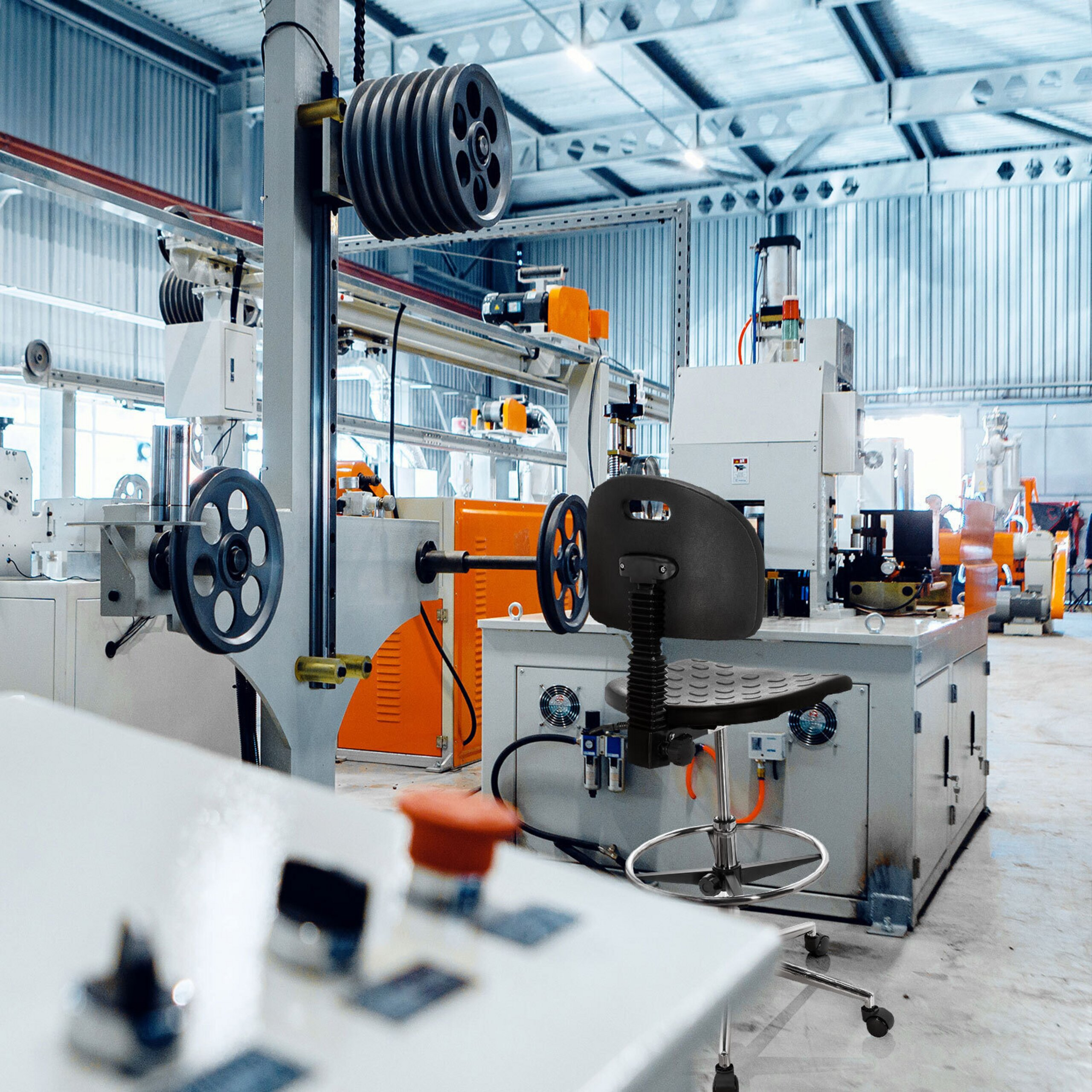 Industrielle Fabrikhalle mit Maschinen und einem schwarzen Bürostuhl im Vordergrund.