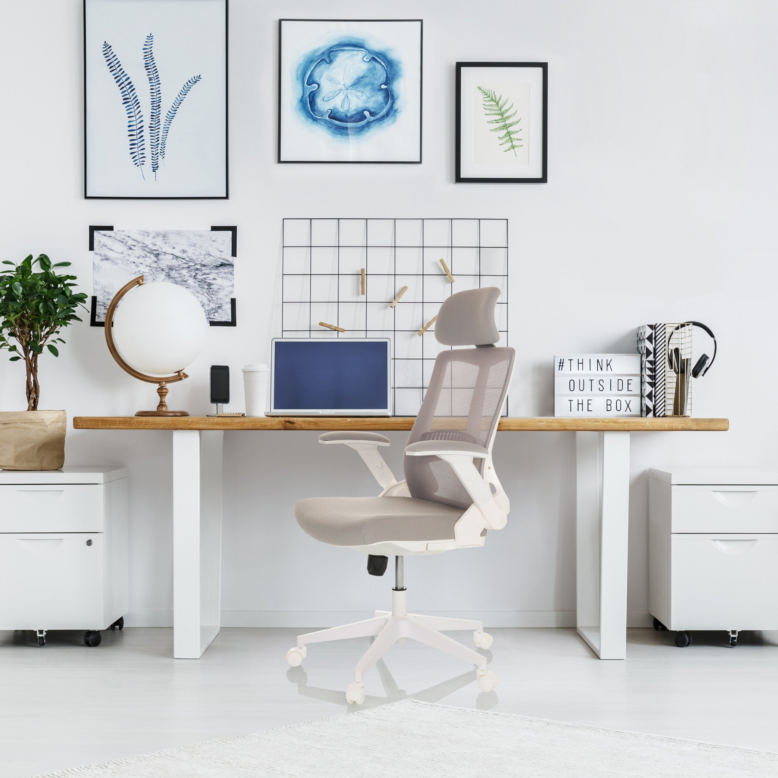 Moderne Schreibtisch-Einrichtung mit einem grauen Stuhl, Laptop, Globus und gerahmter Kunst an einer weißen Wand.