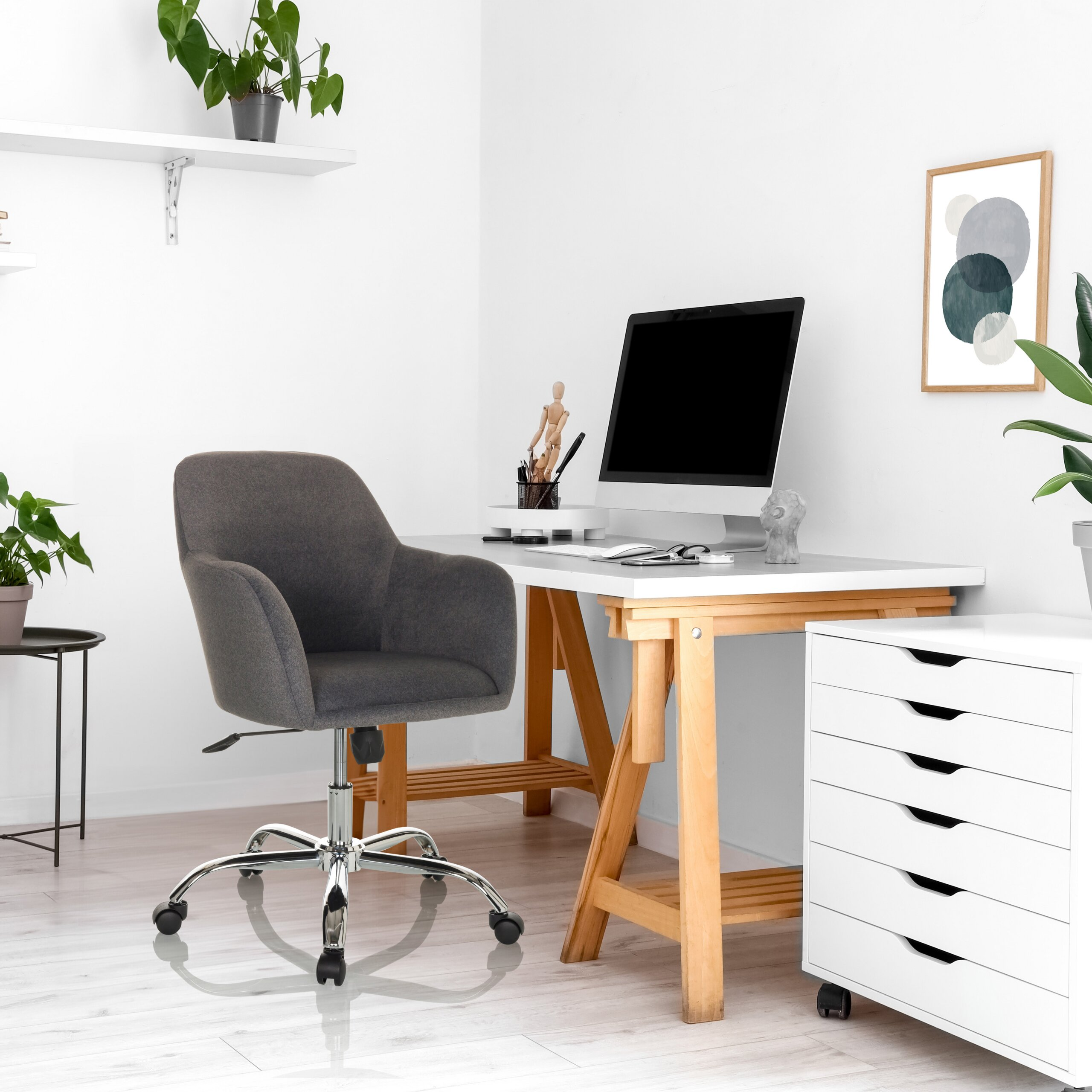 Moderne Schreibtisch-Ecke mit PC, grauem Stuhl, weißem Schrank, Pflanzen und Bild an weißer Wand.