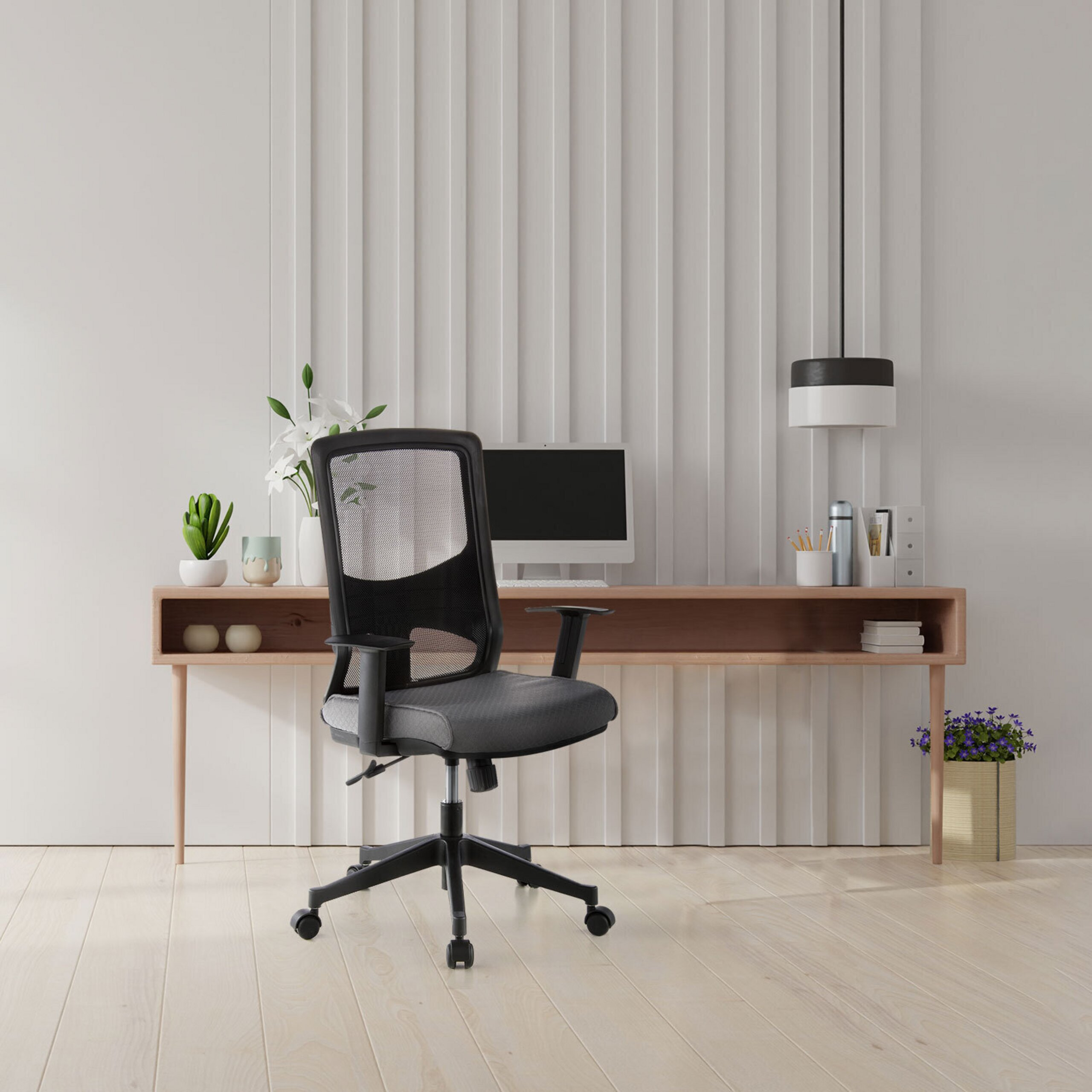 Moderne Büroecke mit schwarzem Drehstuhl, Holztisch, Computer, Blumen und Lampe vor weißer Wand.