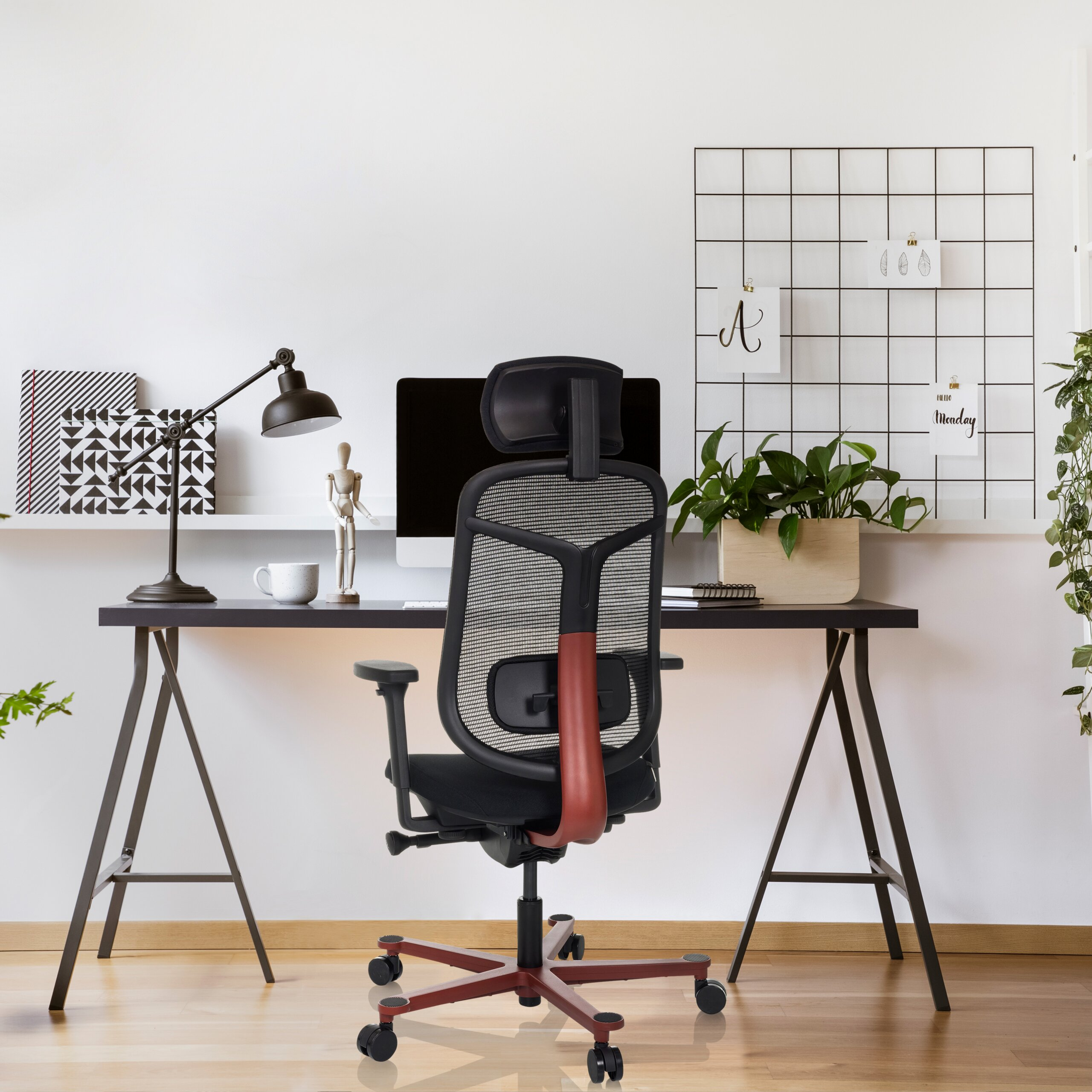 Ein modernes Homeoffice mit schwarzem ergonomischen Netzstuhl, Schreibtisch mit Computer, Lampe, Pflanze und Wandgitter.