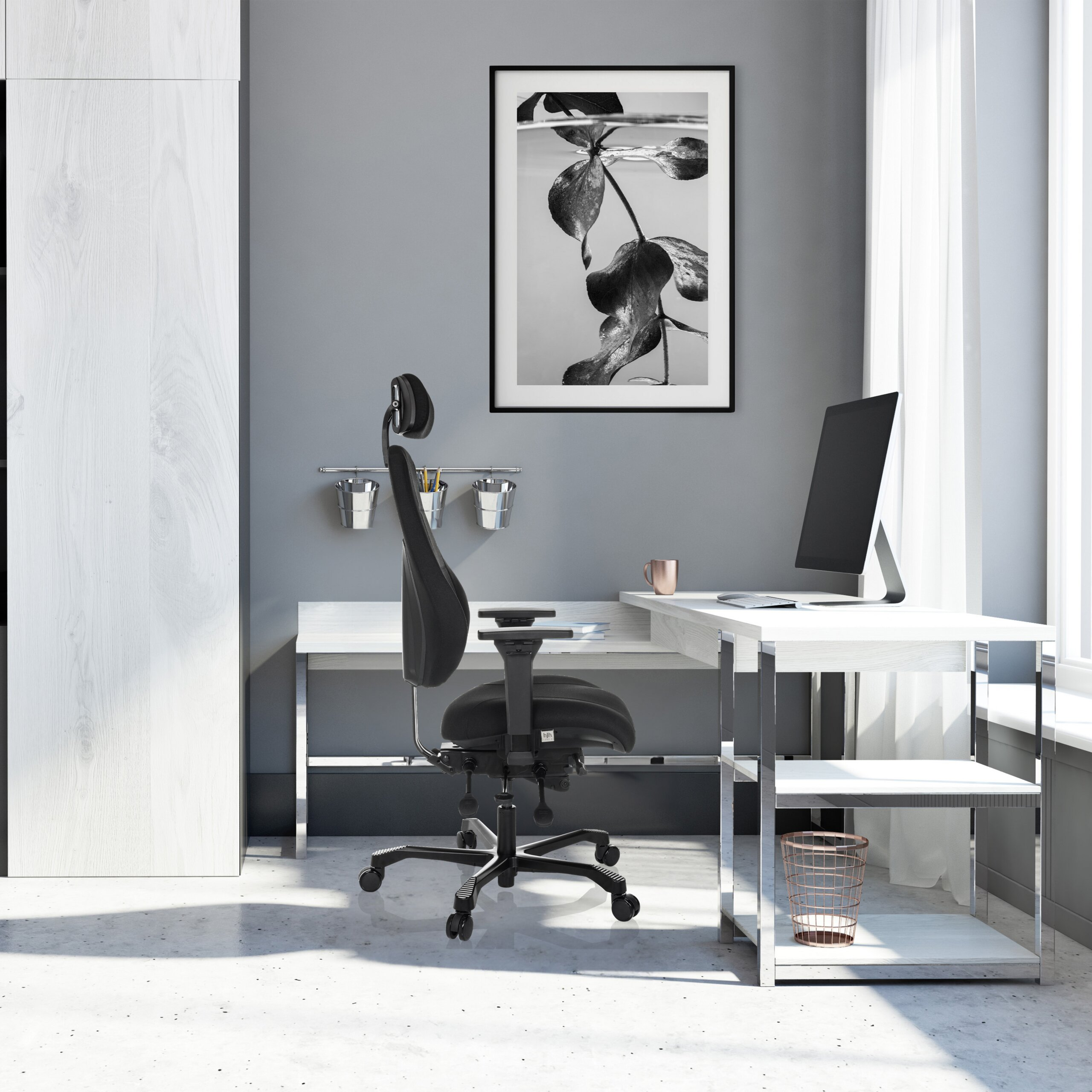 Moderne Büroecke mit weißem Schreibtisch, schwarzem Drehstuhl, Computer und einem großen Schwarz-Weiß-Bild an grauer Wand.