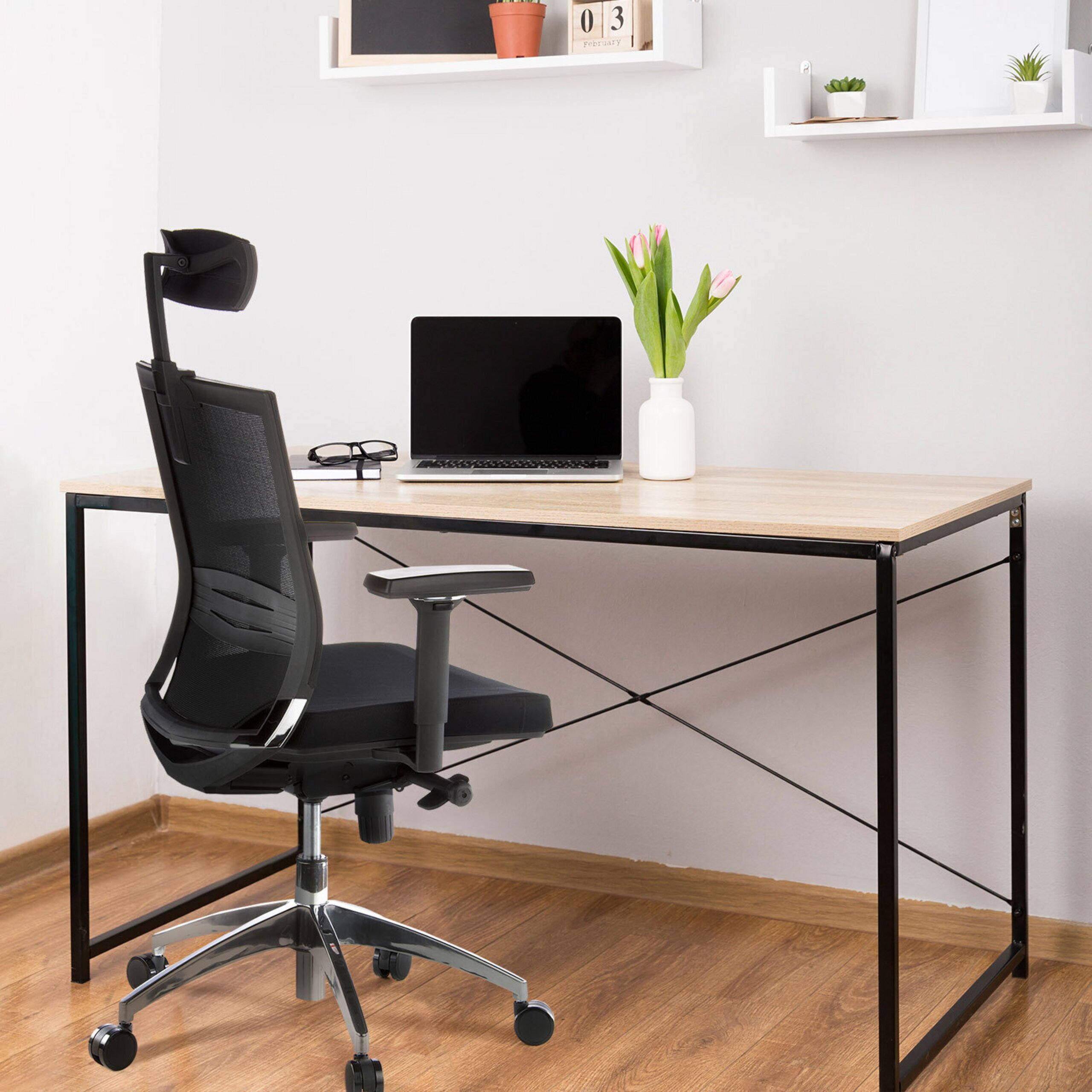 Ein moderner Schreibtisch mit Laptop, Vase mit rosa Tulpen und ein schwarzer Bürostuhl vor einer weißen Wand.
