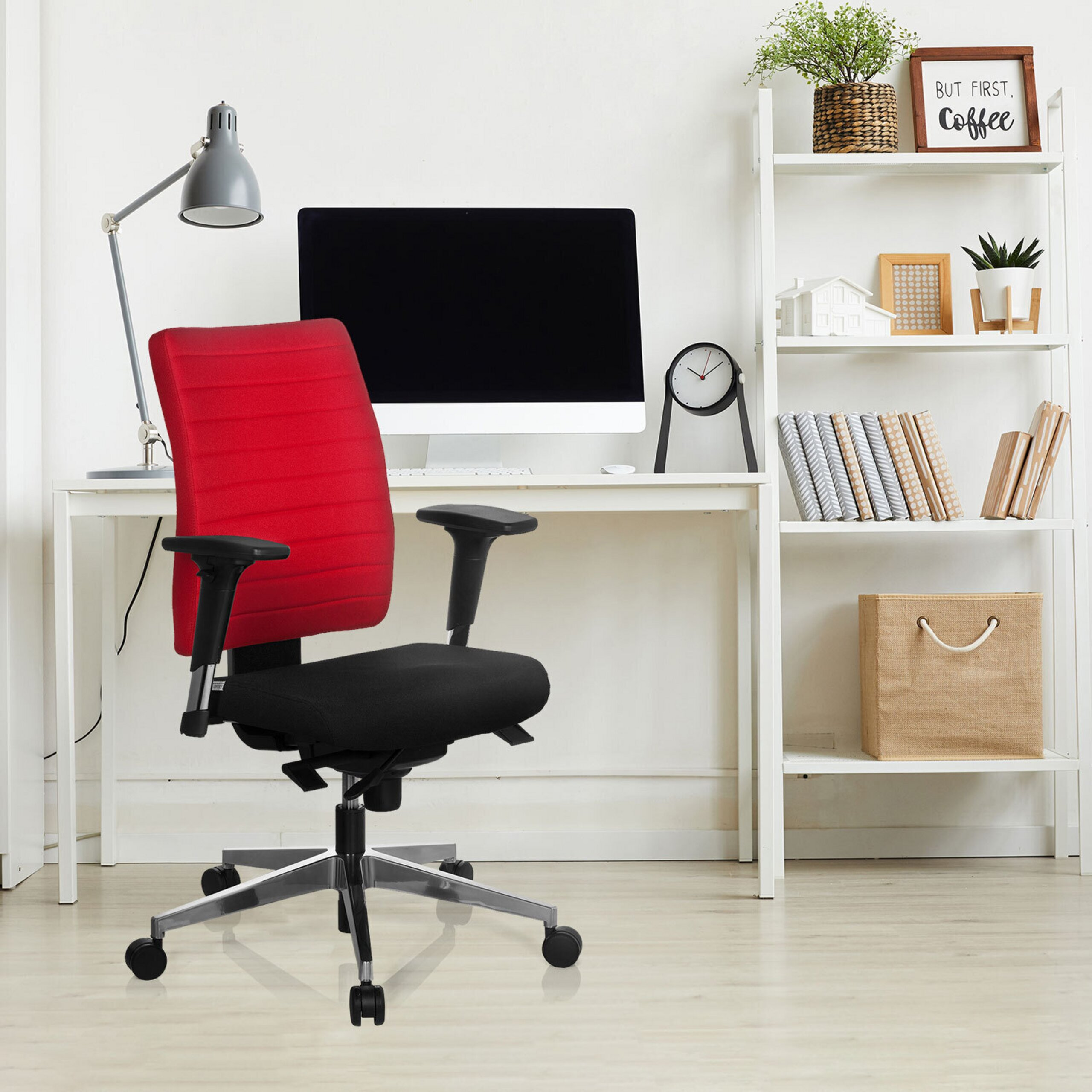 Moderner Arbeitsplatz mit rot-schwarzem Drehstuhl im Vordergrund, weißem Schreibtisch, Computer und Regal.